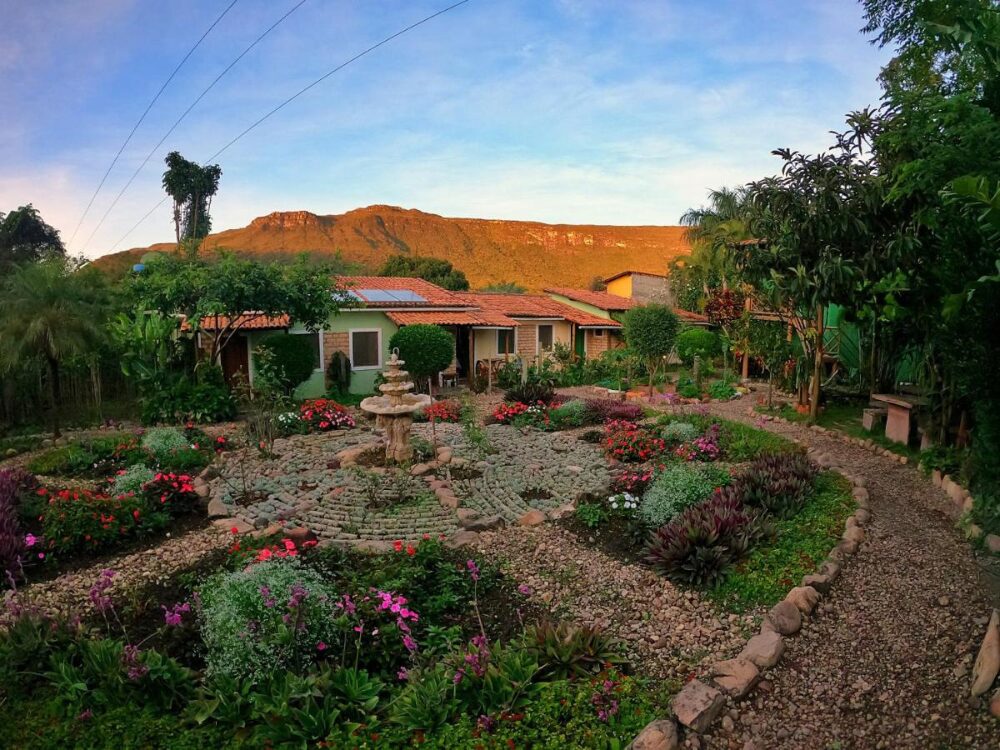 A well-kept circular garden with a stone fountain at a peaceful retreat, framed by green mountains in Chapada Diamantina. 