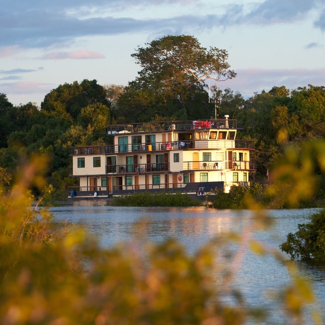 The La Jangada chic catamaran sailing on the Amazon river, surrounded by trees, offering a blend of comfort and adventure.