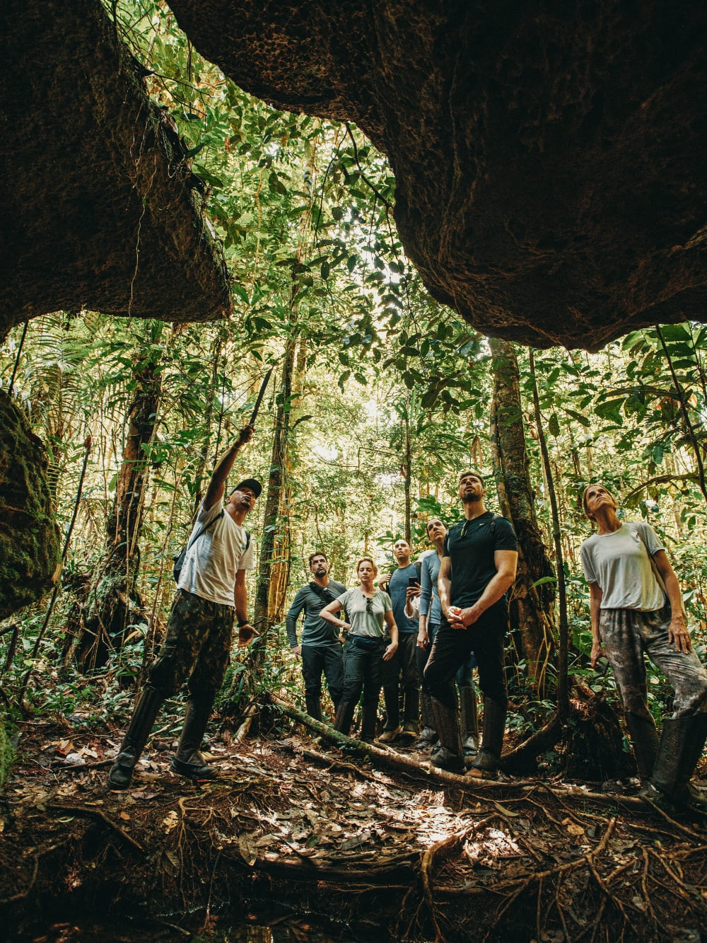 Group of tourists exploring a cave formation within the Amazon rainforest, looking out at the jungle with an expert local guide.