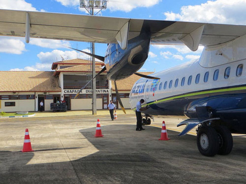 Azul airline plane parked on the runway at Chapada Diamantina airport. Employees work near the aircraft on a sunny day.