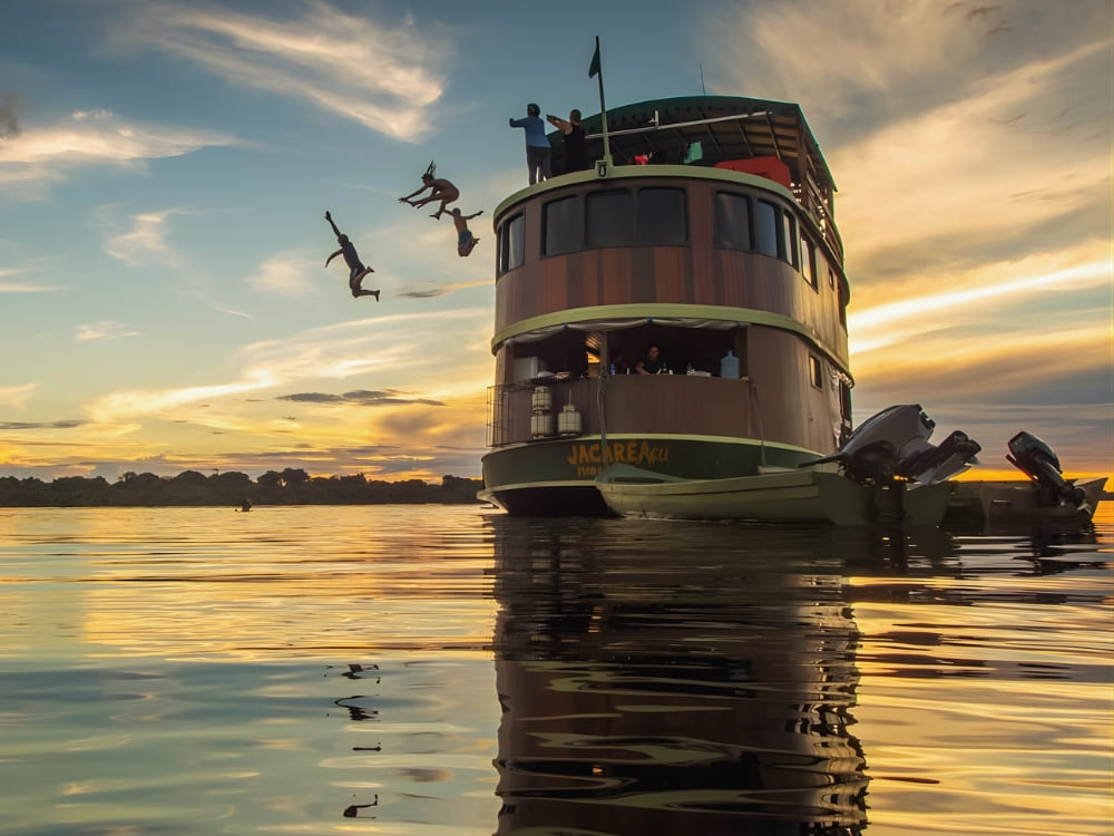 Travelers jumping from the top deck of a river cruise boat into the Amazon River at sunset during an adventurous ecotourism trip