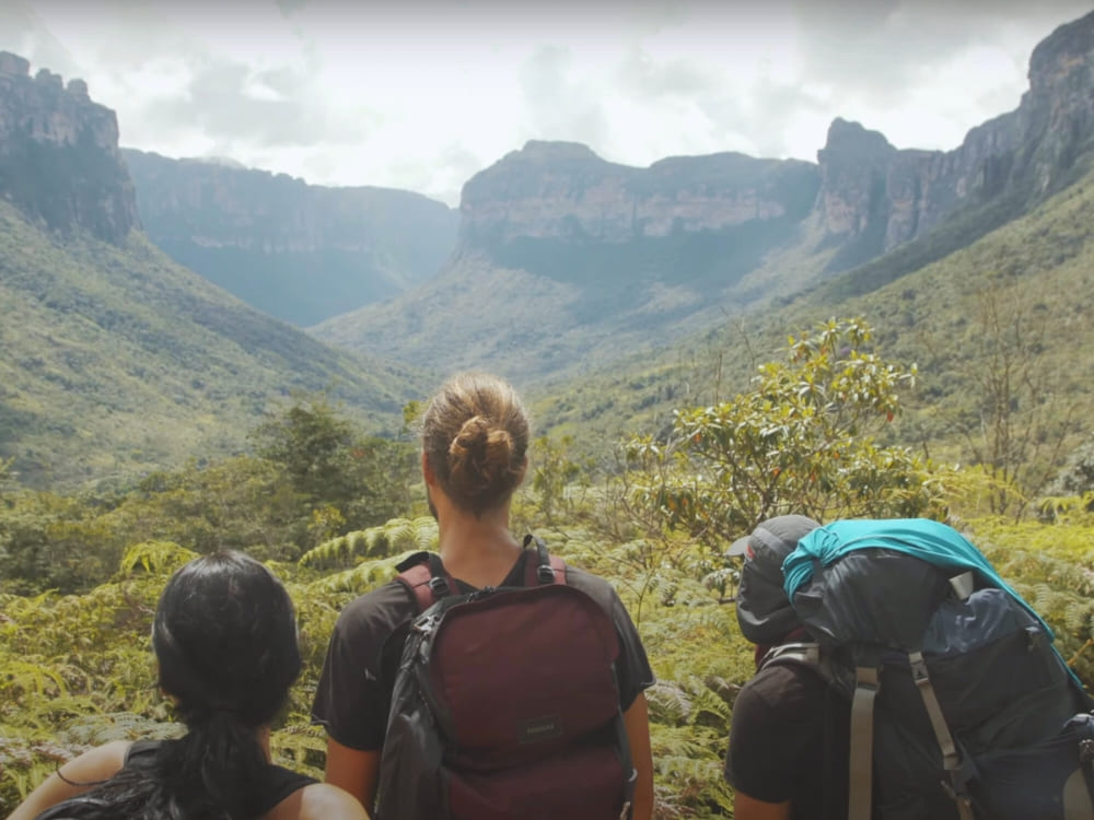 Three travelers with backpacks looking out over a vast green valley deep inside Chapada Diamantina. 