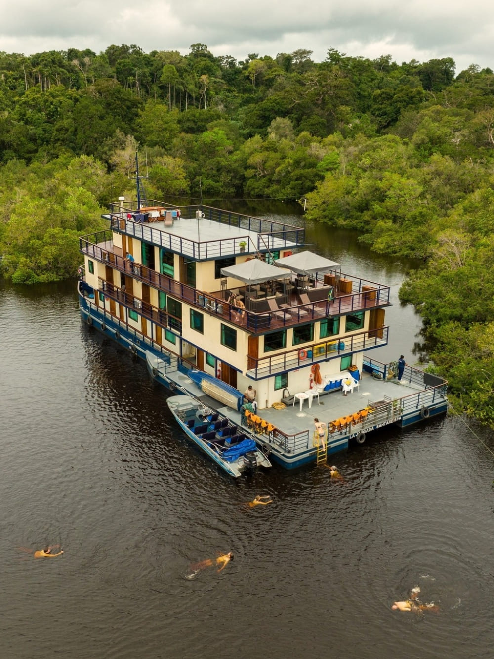 Aerial view of the La Jangada riverboat docked near the jungle, showcasing its spacious upper deck and proximity to the rainforest nature.