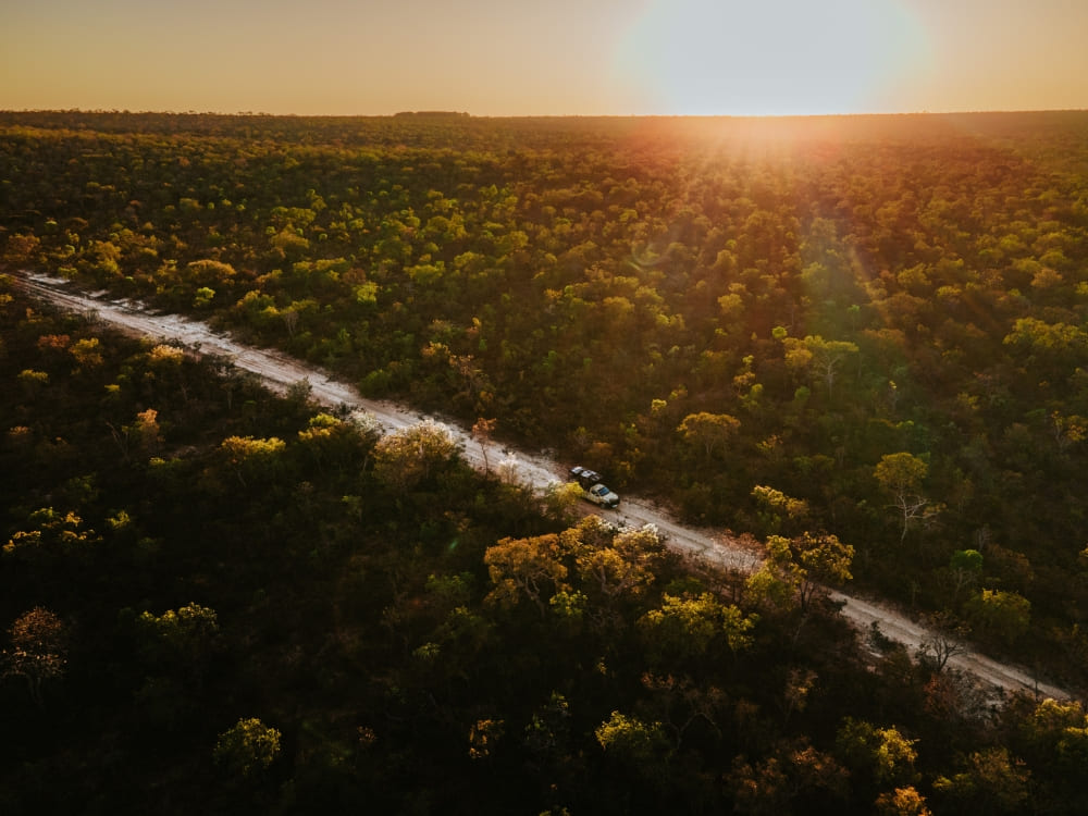 An off-road vehicle driving on a dirt road through the vast Cerrado plains illuminated by the golden sunset light.