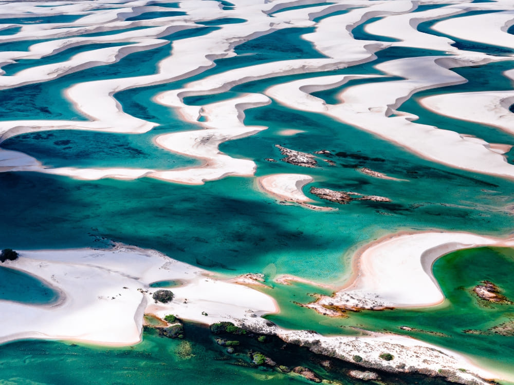 Aerial view of vibrant blue pools nestled among stark white sand dunes, highlighting the Lençóis Maranhenses best time to visit lagoons months. 