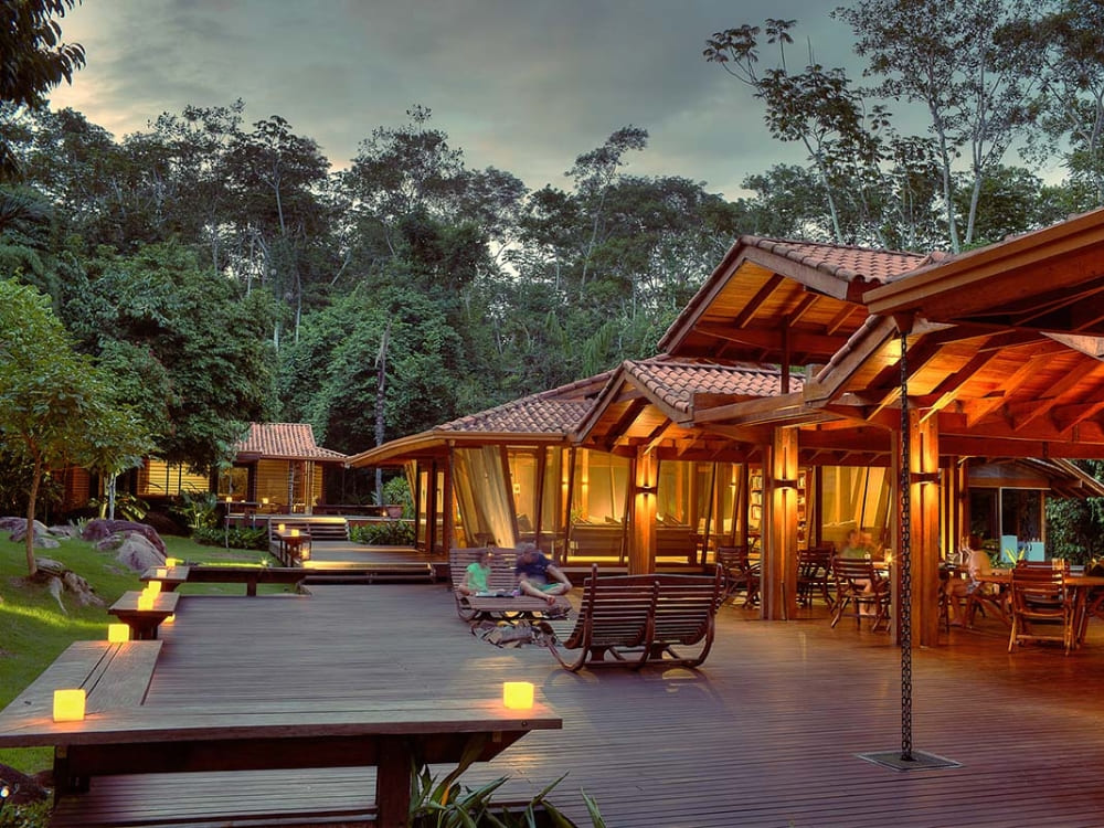 A wooden deck illuminated by small lights at dusk, surrounded by the lush tropical vegetation of the rainforest.