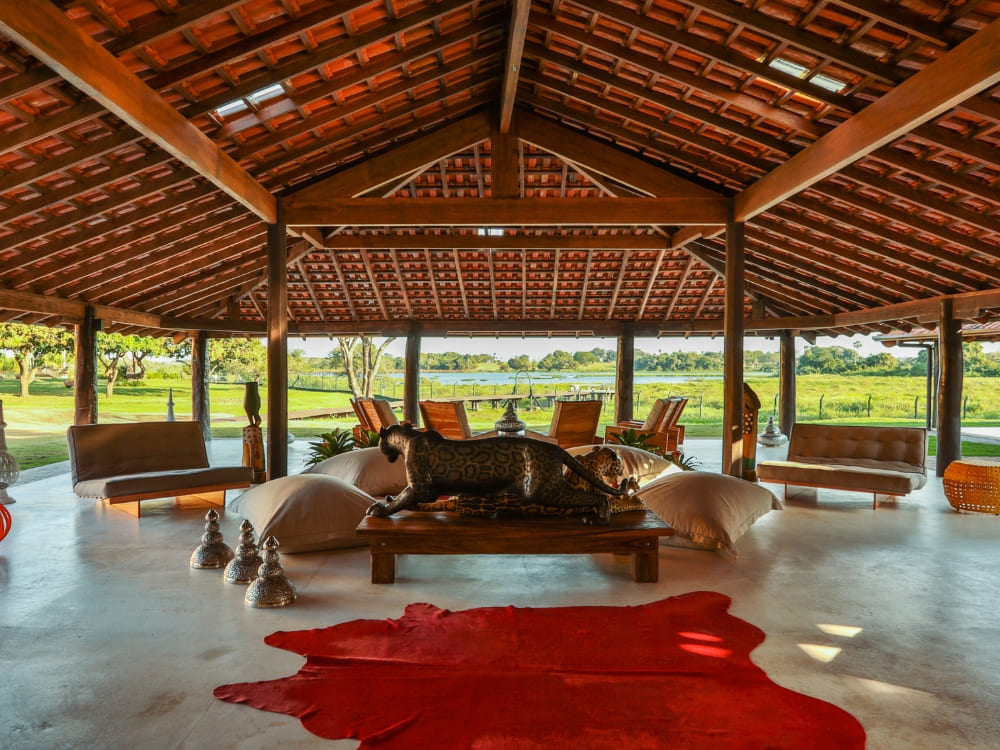 Open-air living room featuring a red cowhide rug and a carved wooden jaguar at Caiman ecolodge.