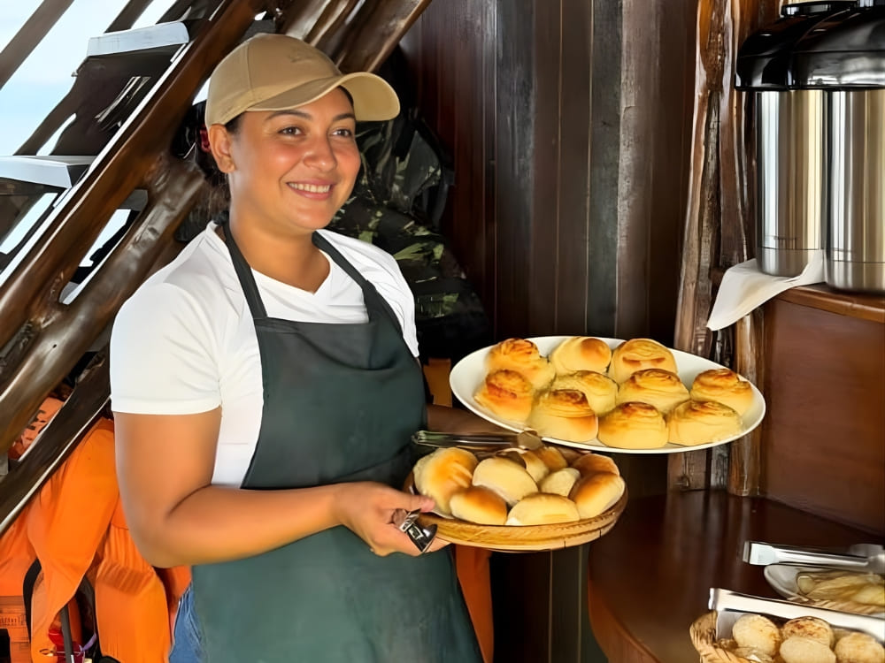 Woman in an apron holding plates with fresh bread on a vessel, representing the female financial independence achieved through tourism.