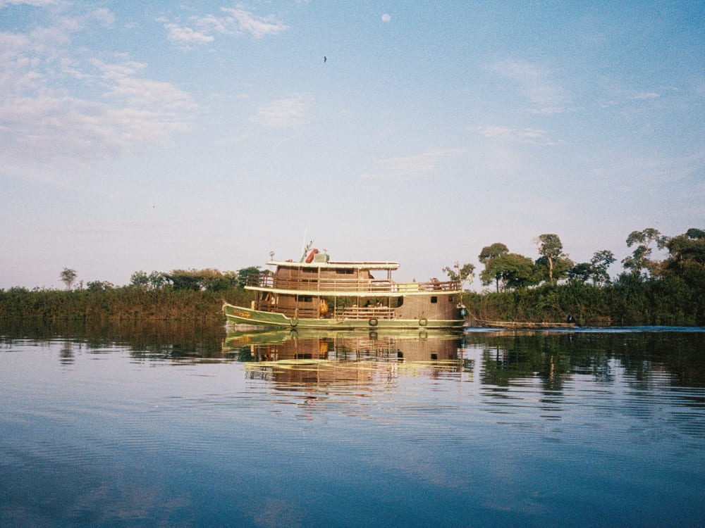 Traditional river cruise boat navigating the calm waters of the Rio Negro, with green vegetation reflecting on the water.