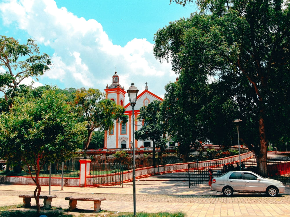 White and orange historic church with a curved ramp surrounded by green trees in a quiet Manaus city plaza. White and orange historic church with a curved ramp surrounded by green trees in a quiet Manaus city plaza.