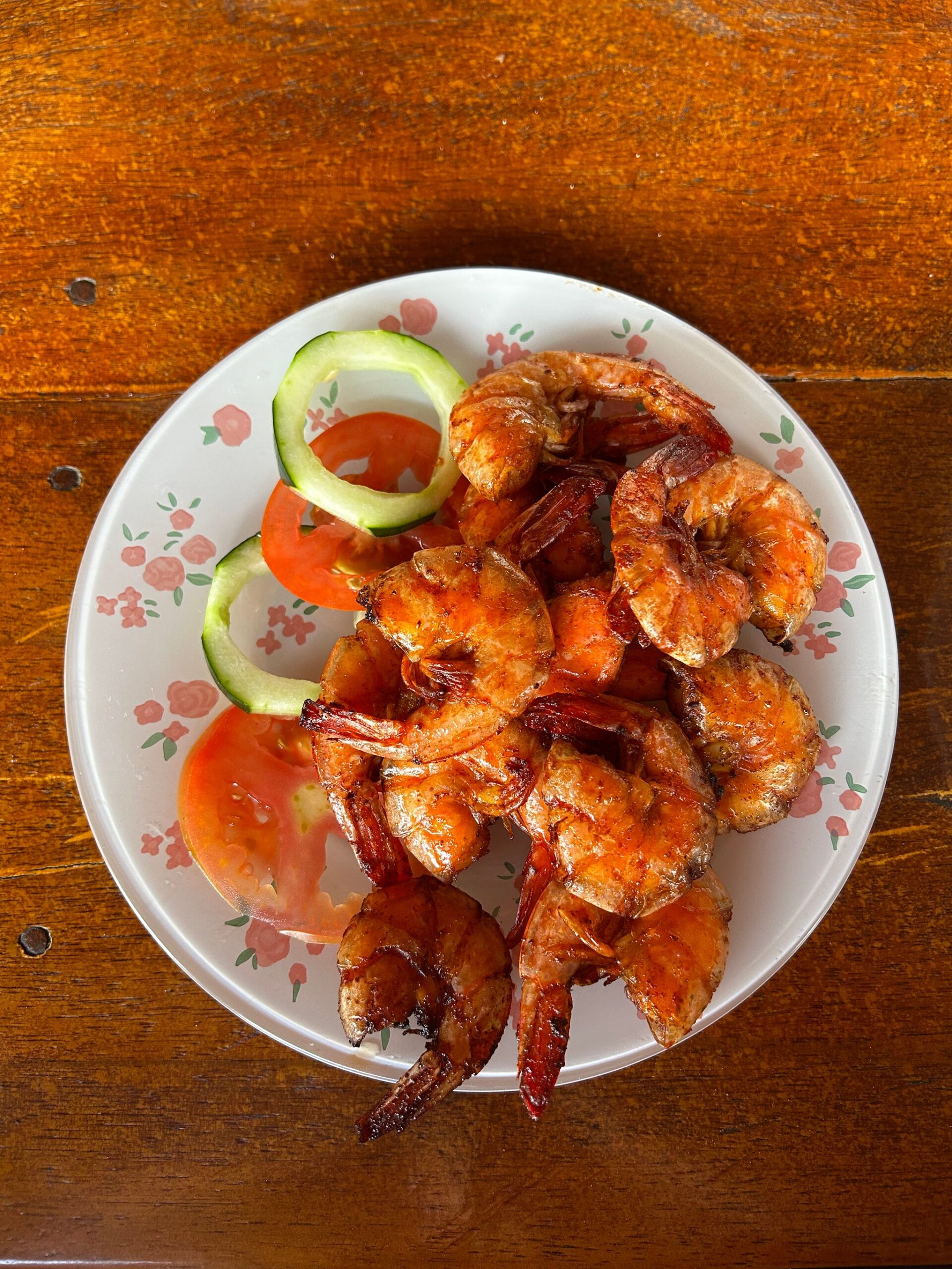 Draufsicht auf einen Teller mit gegrillten ganzen Garnelen, Tomaten- und Gurkenscheiben auf einem geblümten Teller, serviert in einem lokalen Restaurant in der Region Lençóis Maranhenses