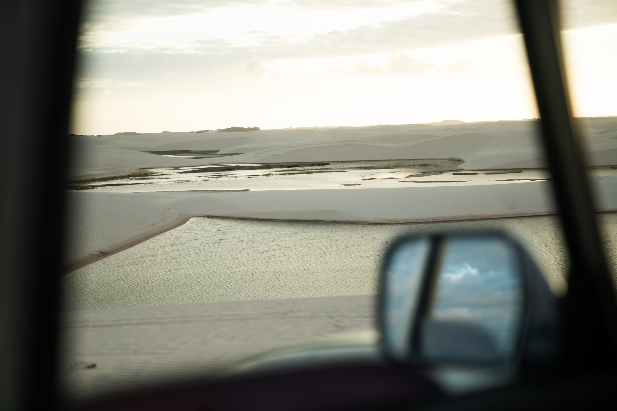 Weiße Sanddünen und flache Regenwasserlagune in Lençóis Maranhenses, gesehen durch das Fenster eines Geländefahrzeugs mit Außenspiegel im Vordergrund