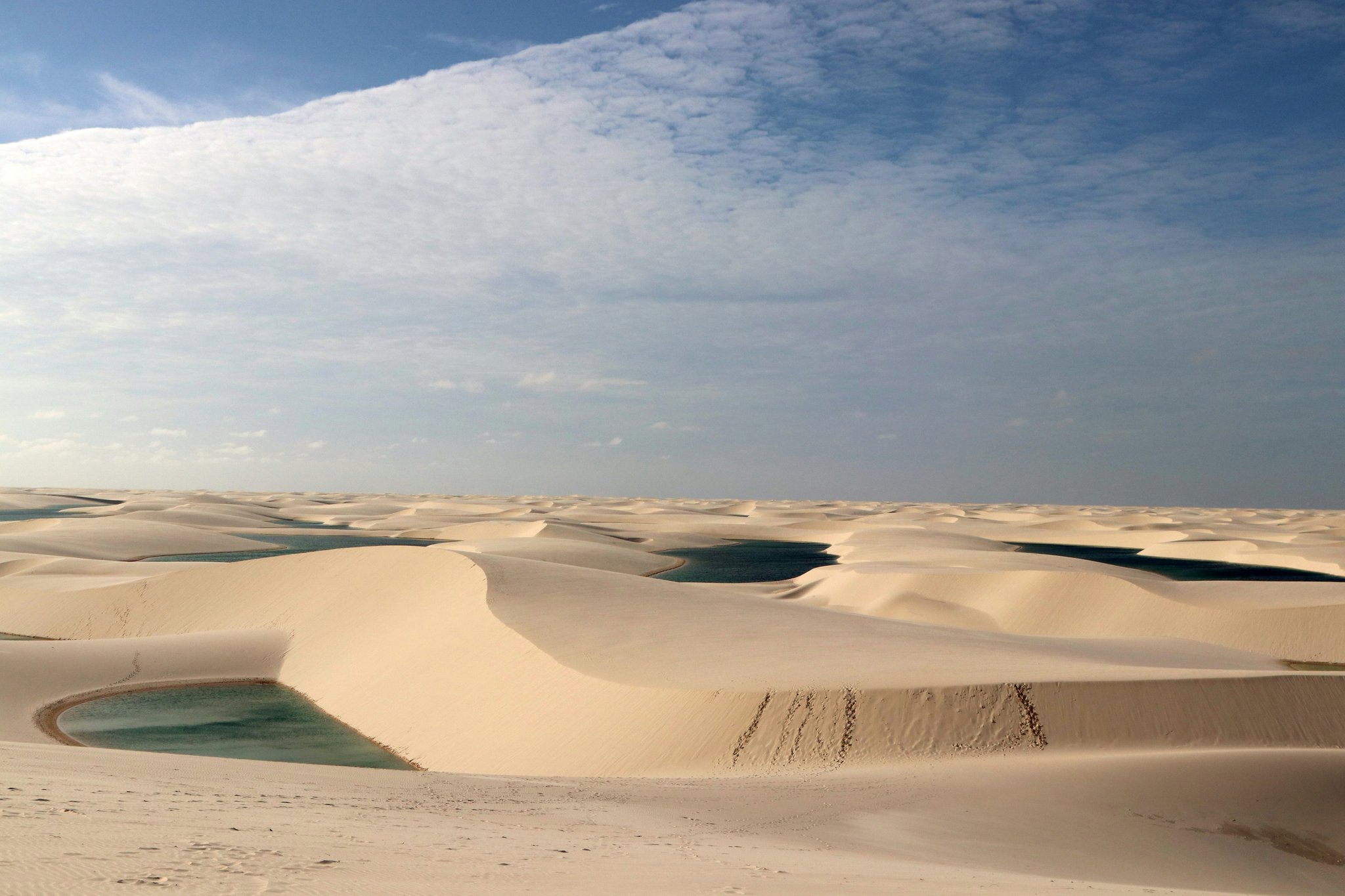 Weitläufige weiße Sanddünen der Lençóis Maranhenses erstrecken sich bis zum Horizont, mit mehreren türkisfarbenen Regenwasserlagünen zwischen den Dünenkämmen unter einem weiten blauen Himmel