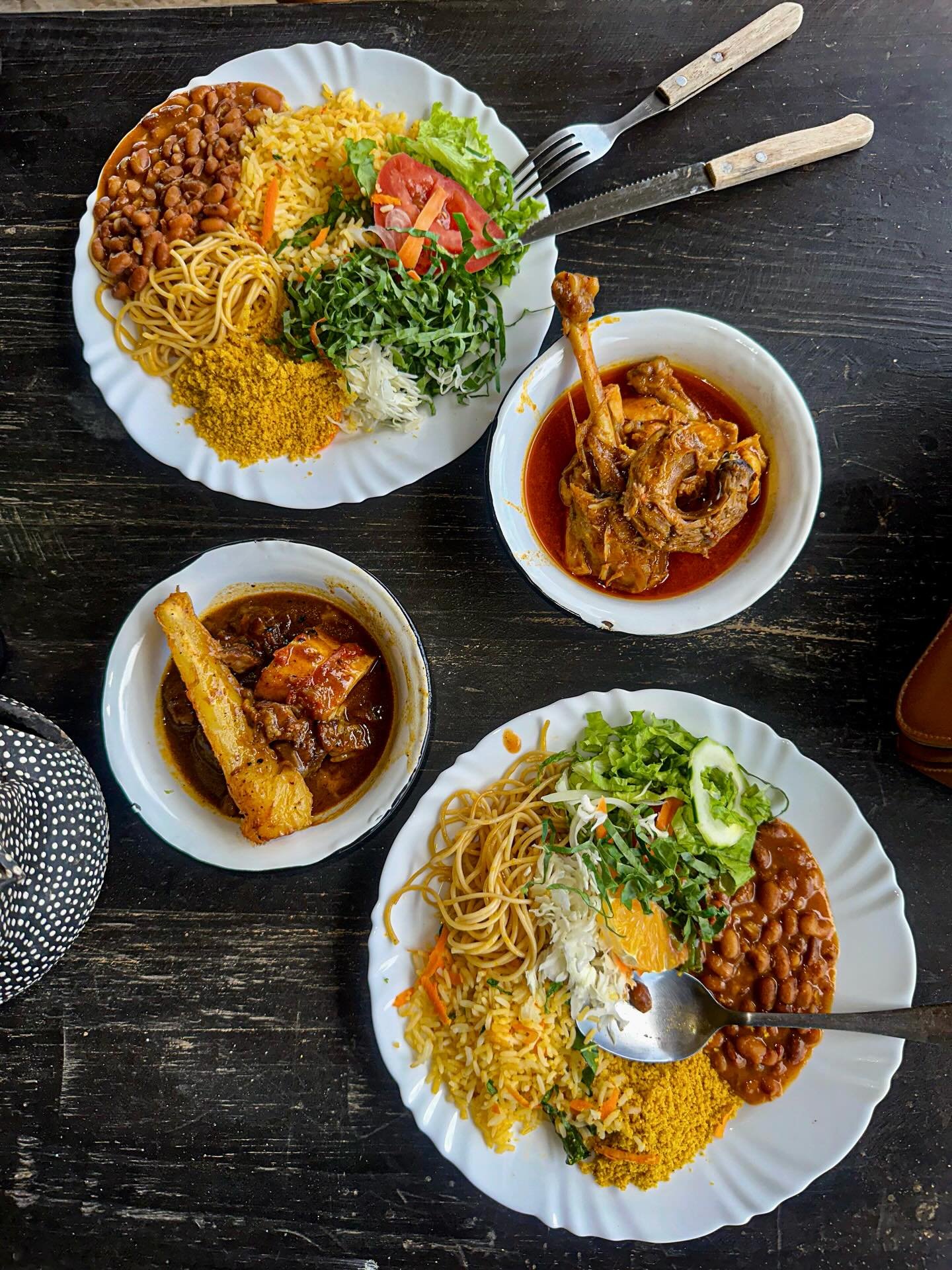 Draufsicht auf zwei üppige Teller mit Reis, Farofa, Nudeln, Bohnen und frischem Salat sowie zwei Schälchen mit geschmortem Fleisch in kräftiger Soße, serviert in einem lokalen Restaurant nahe Lençóis Maranhenses Santo Amaro
