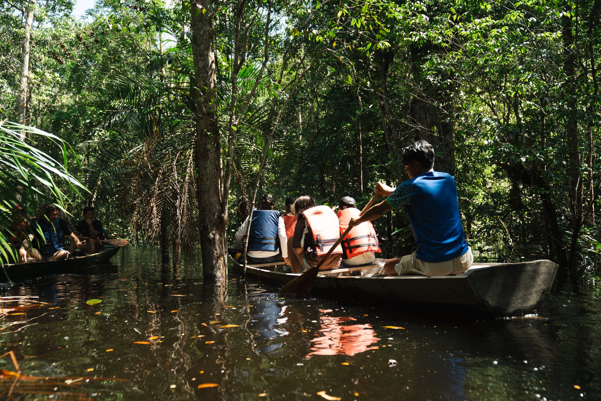 Op een paar centimeter boven het water zie je het regenwoud van zijn rustige kant. Gasten met reddingsvesten peddelen in houten kano's door een ondergelopen igapó-woud tijdens een Amazon Turtle Lodge excursie