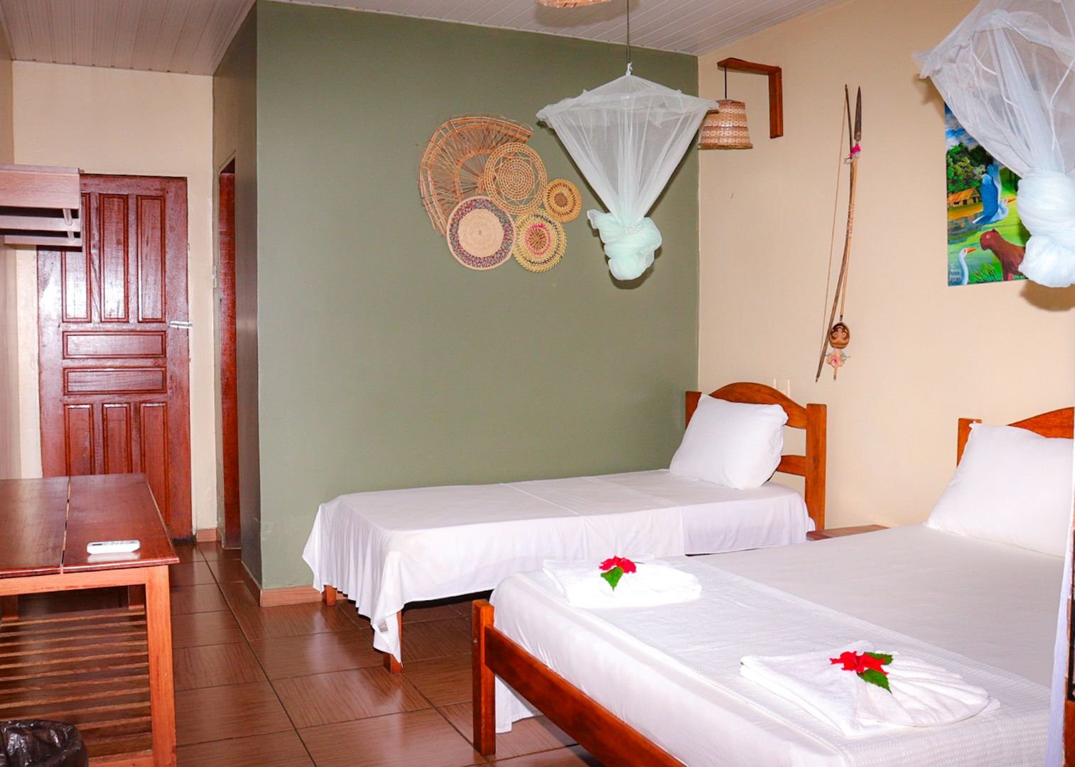 Rustig, verzorgd, en precies wat je nodig hebt na een dag in het oerwoud. Tweepersoonskamer in de Amazon Turtle Lodge met witte beddengoed, hangende klamboes, gevlochten muurdecoraties en bloemetjes handdoekvouwsel op het bed