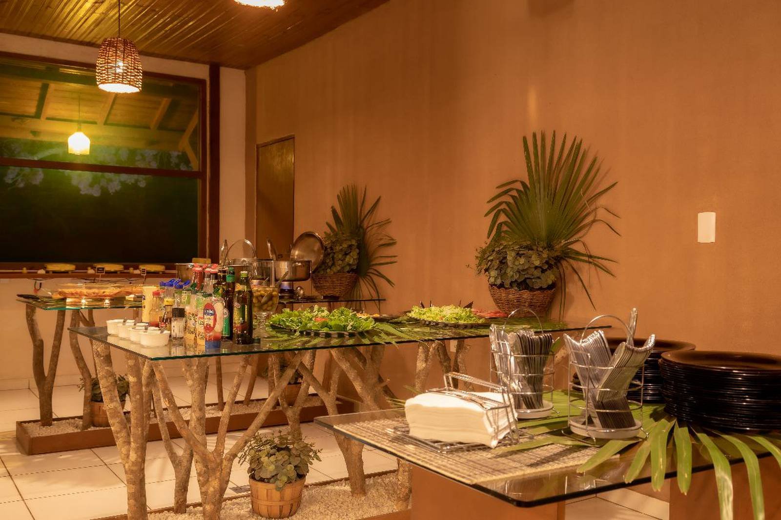 Binnenbuffet in een budgetvriendelijke Pantanal-lodge, met glazen tafels op rustieke takpoten, volgeladen met salades, condimenten, warme gerechten in stalen potten en tropische planten onder warm hanglamplicht