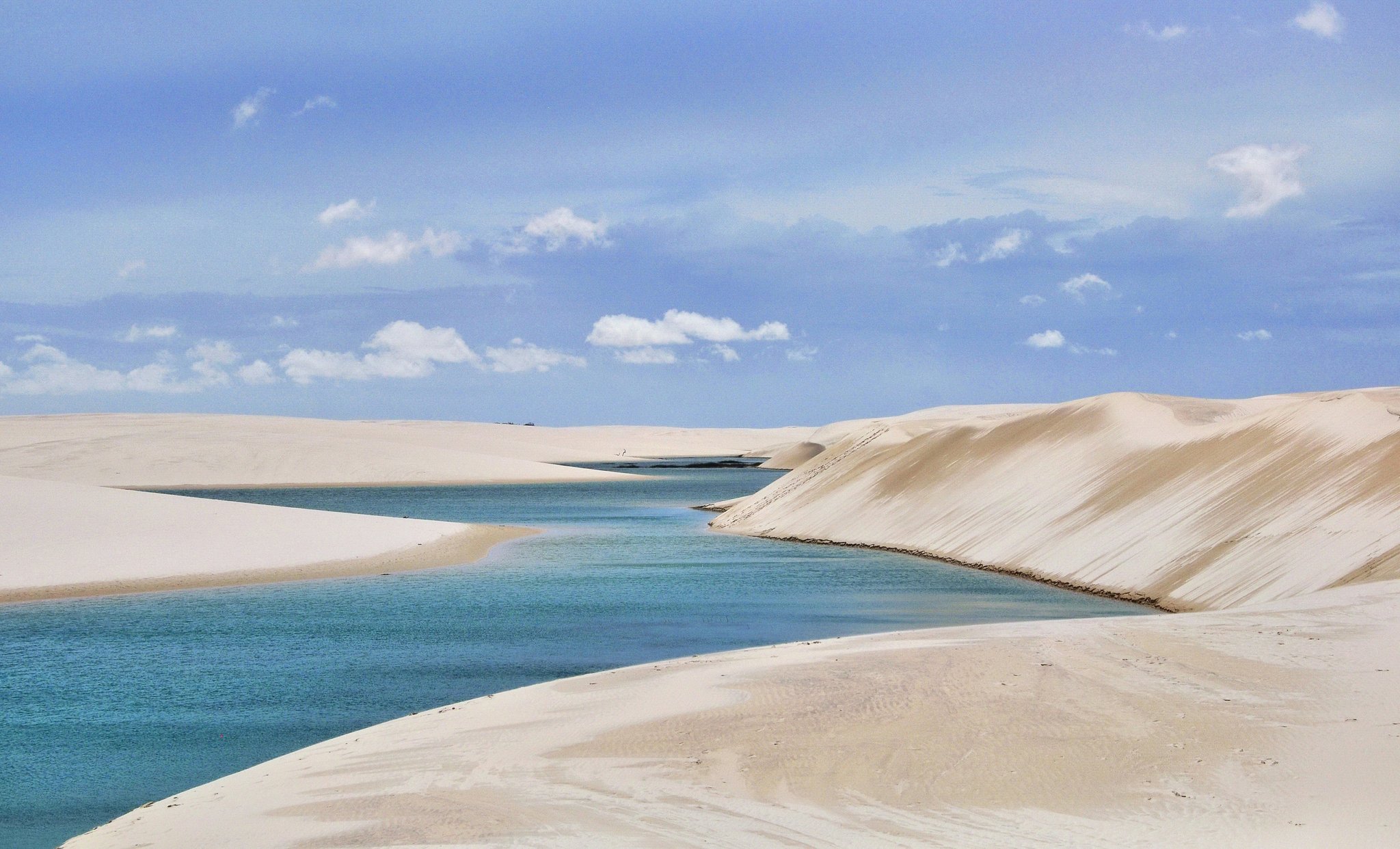 Türkisfarbene Regenwasserlagune zwischen weißen Sanddünen unter blauem Himmel in Lençóis Maranhenses bei Santo Amaro