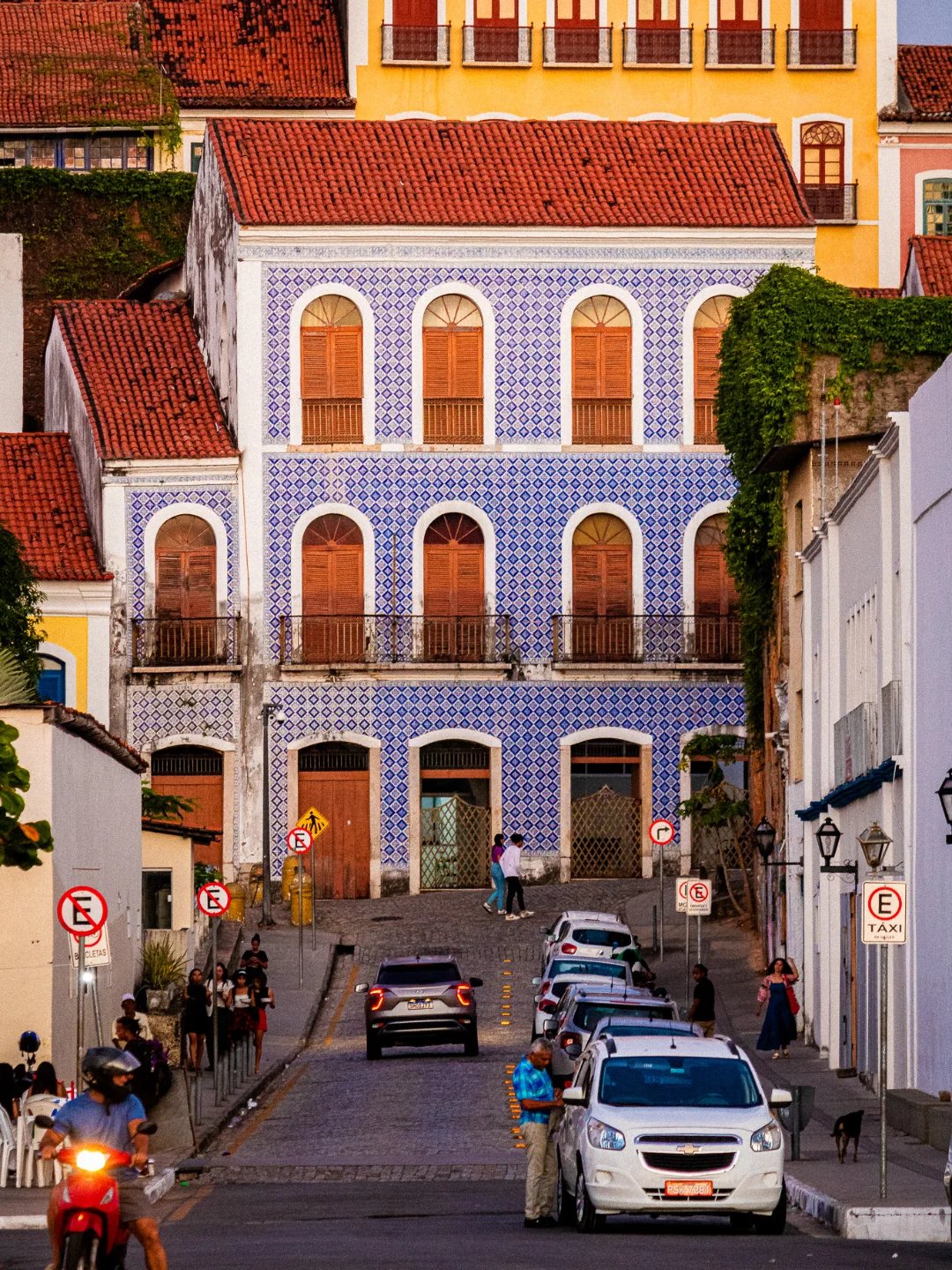 Dreigeschössiges Kolonialgebäude mit blau-weißen portugiesischen Azulejos an einer Kopfsteinpflasterstraße in Santo Amaro, mit bunten Nachbarfassaden und Einheimischen im warmen Abendlicht