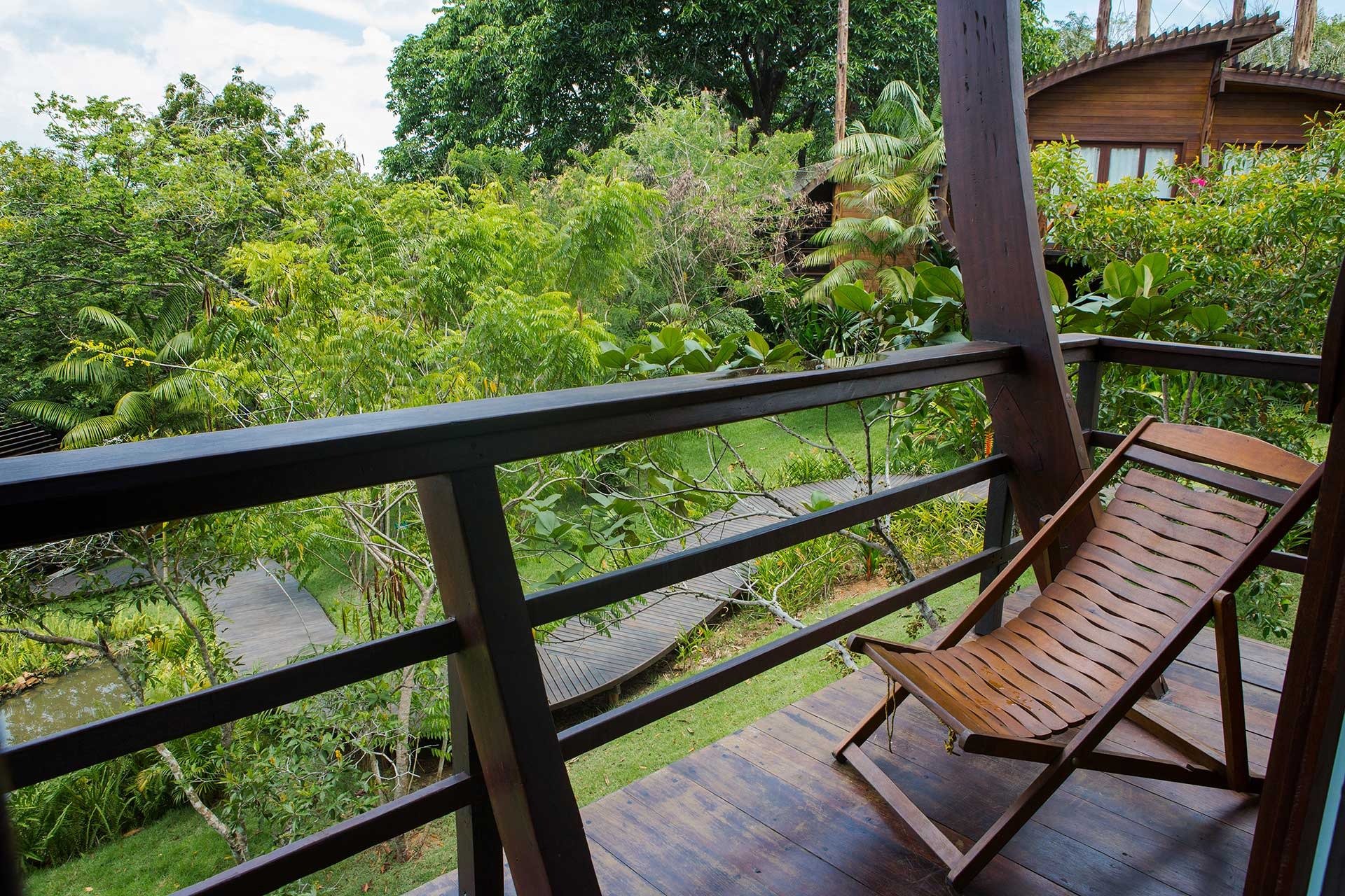 Geen haast hier, de jungle heeft alle tijd. Een houten ligstoel op het terras van Mirante do Gavião met uitzicht op een weelderige tropische tuin, vlonderpad en aangrenzend houten bungalow
