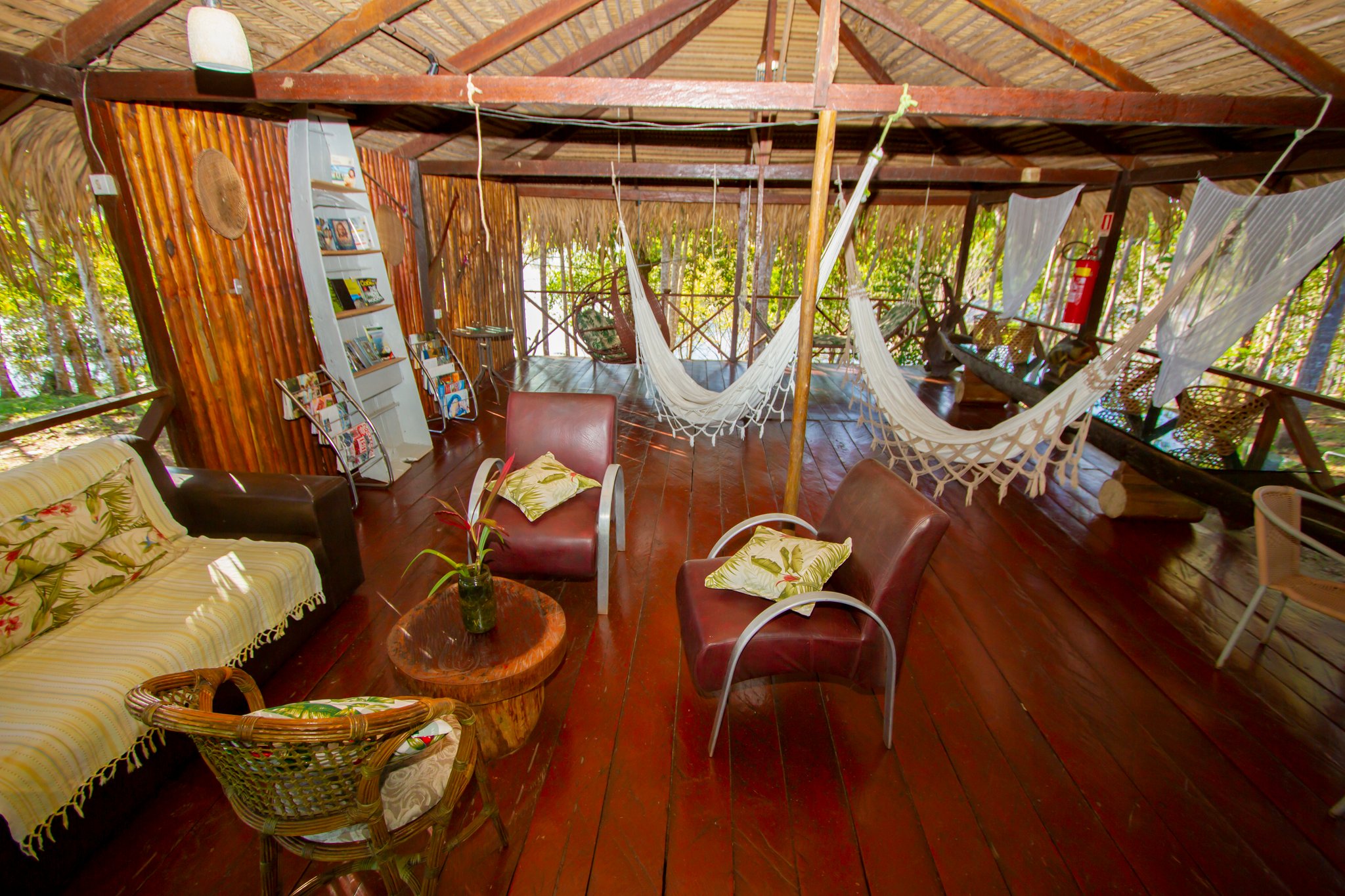 Hangmat kiezen, boek pakken, het regenwoud neemt het over. Openlucht gemeenschappelijke lounge van de Amazon Turtle Lodge met geweven hangmatten, leren fauteuils en een gepolijste hardhouten veranda omringd door regenwoud