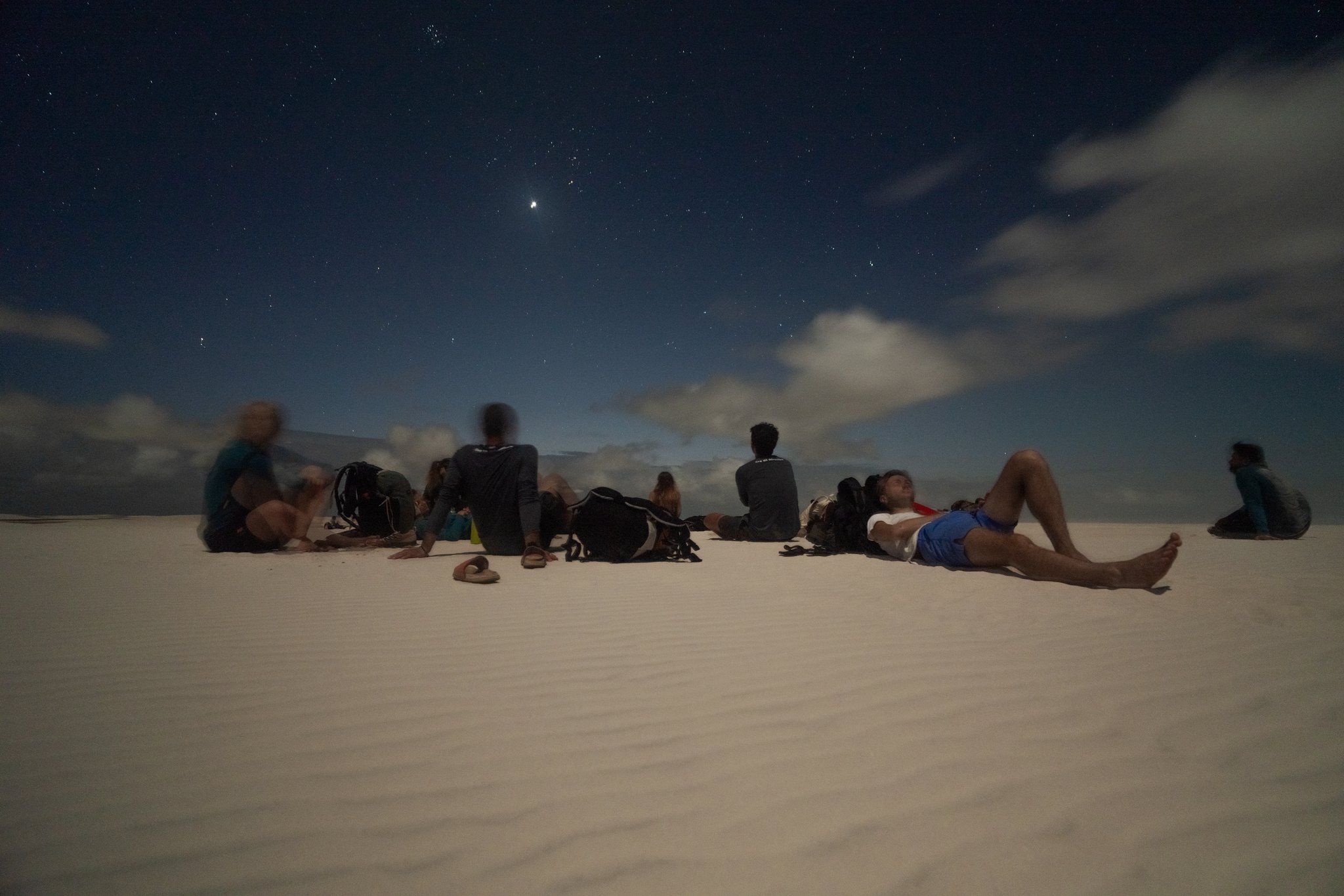 A group of travelers lying and sitting on white sand dunes at night beneath a star-filled sky, part of a Lençóis Maranhenses full itinerary stargazing experience