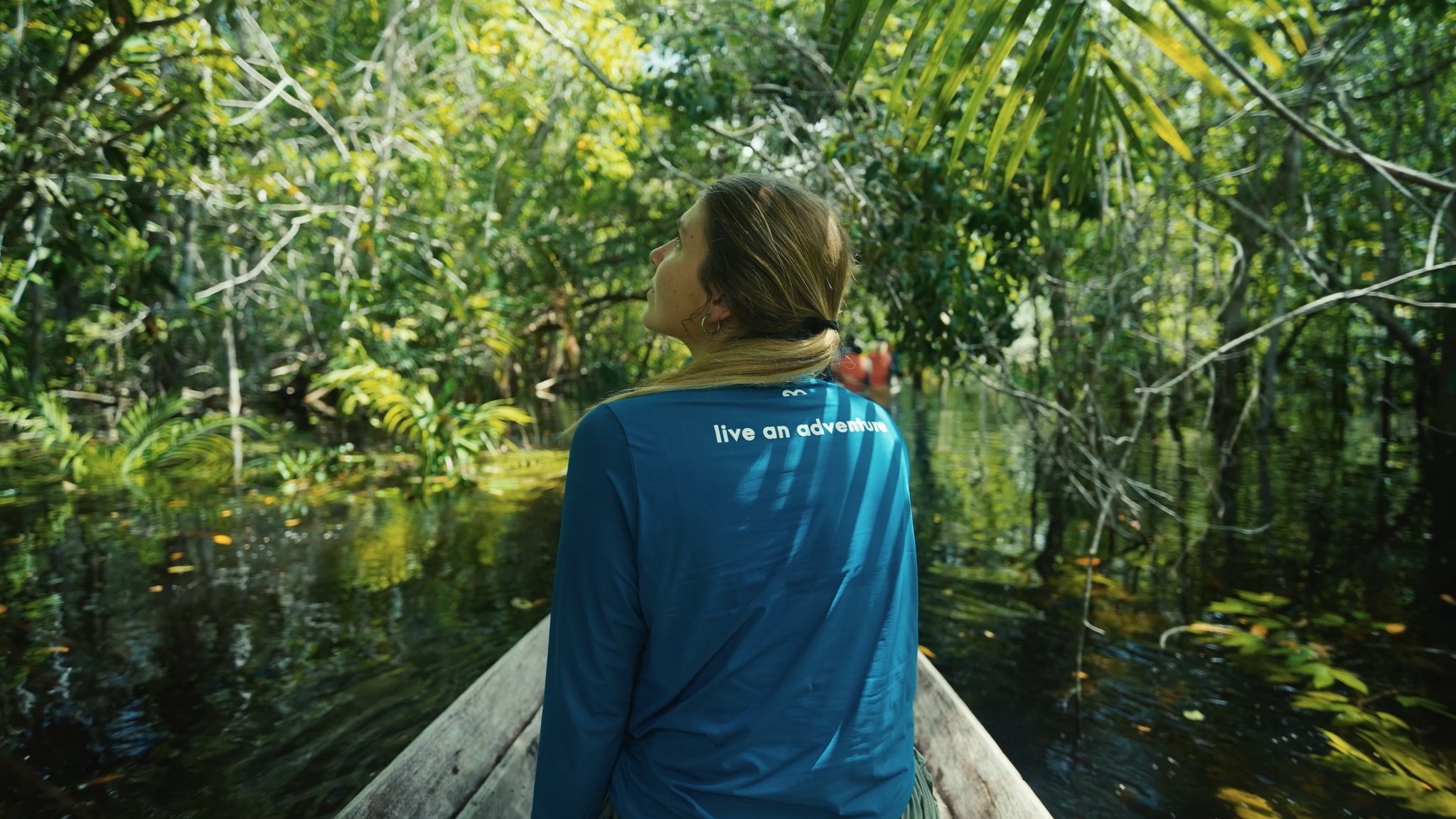 Geen kaart, geen haast. Het oerwoud bepaalt het tempo. Een reizigster zit op de boeg van een houten kano en kijkt omhoog naar het dichte, overstroomde igapó-woud tijdens een tocht van Mirante do Gavião Amazon Lodge, het donkere, tanninerijke water spiegelt het weelderige bladerdak