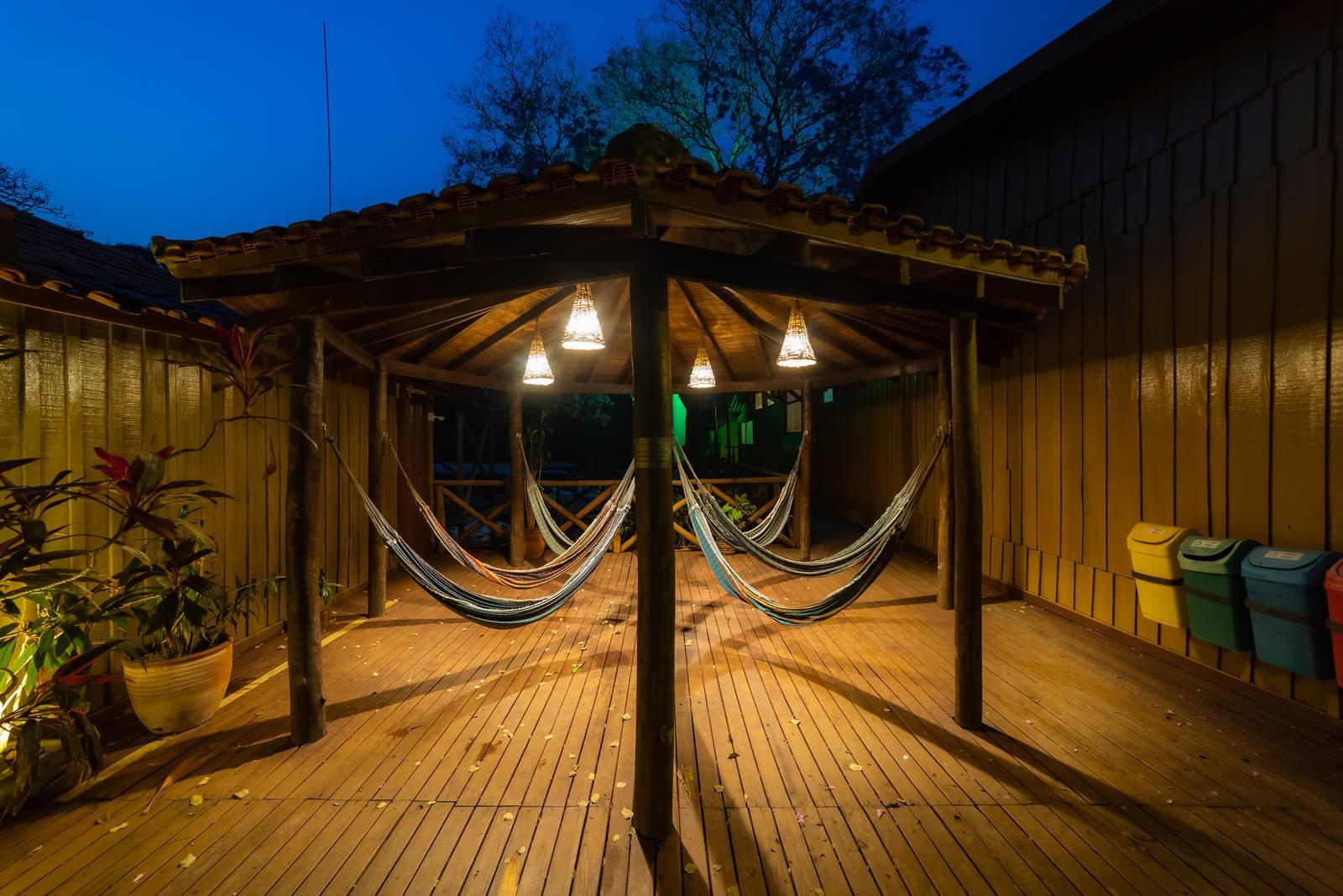 Overdekt houten terras bij schemering tijdens een budget Pantanal tour, met kleurrijke hangmatten onder warme hanglampen en een diepe blauwe avondlucht boven de boomtoppen