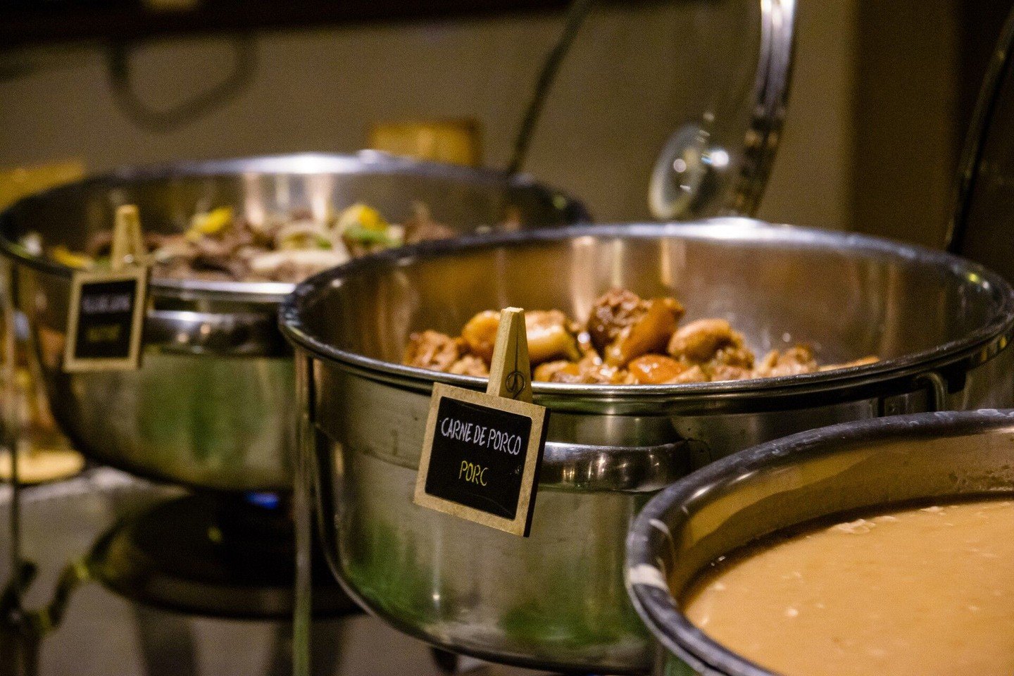 Roestvrijstalen chafing dishes bij een lodgebuffet, de voorste pot gelabeld 'Carne de Porco' gevuld met gestoofde varkensblokjes, onderdeel van de volpension bij deze budget Pantanal tour