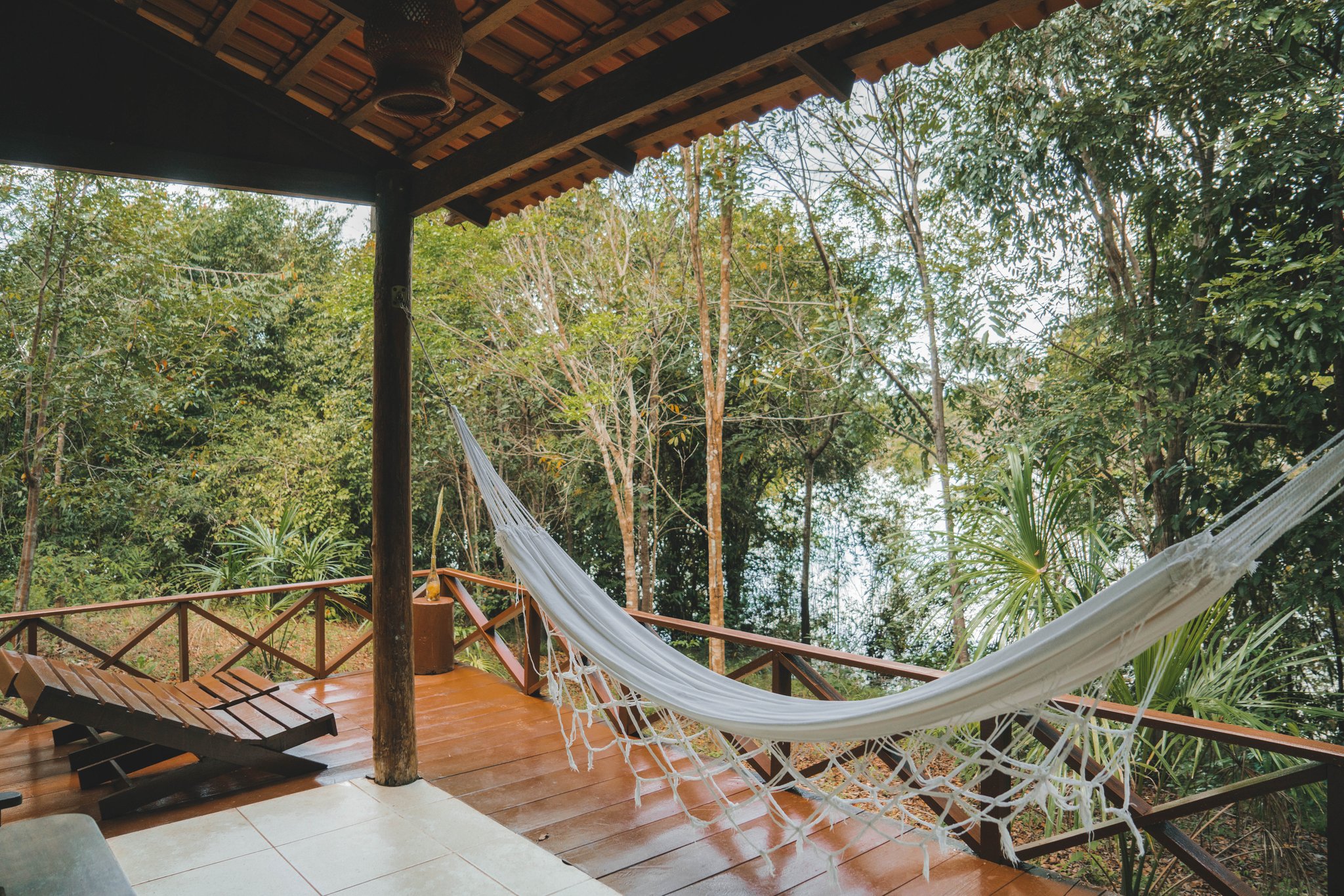 Eén hangmat, eén uitzicht op het regenwoud, geen haast. Een wit touwenhangmat hangt op een hardhouten terras van de Amazon Turtle Lodge, met een houten ligstoel en het weelderige regenwoudgebladerte zichtbaar achter de reling
