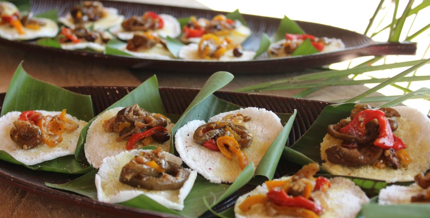 Regional flavours, bite by bite — Pará's ingredients plated with care. Small white cassava rounds topped with sautéed peppers and vegetables, arranged on banana leaves aboard an Amazon cruise from Alter do Chão