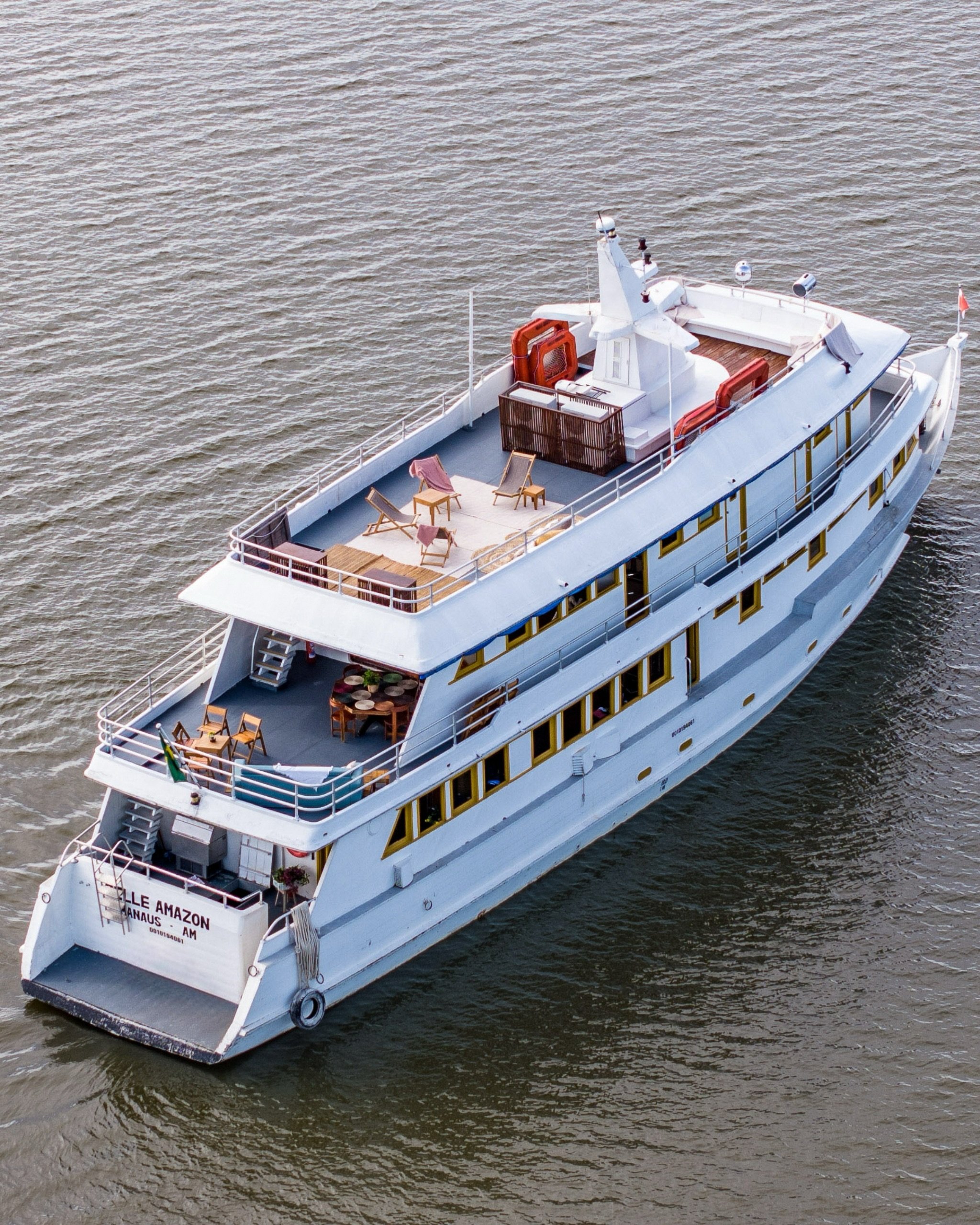 Multi-deck, open terraces, wide brown river — life aboard an Amazon river cruise Brazil travellers remember. Aerial view of the Belle Amazon river cruise vessel underway on the Amazon River, with open sun decks, deck chairs, and dining furniture visible across three levels