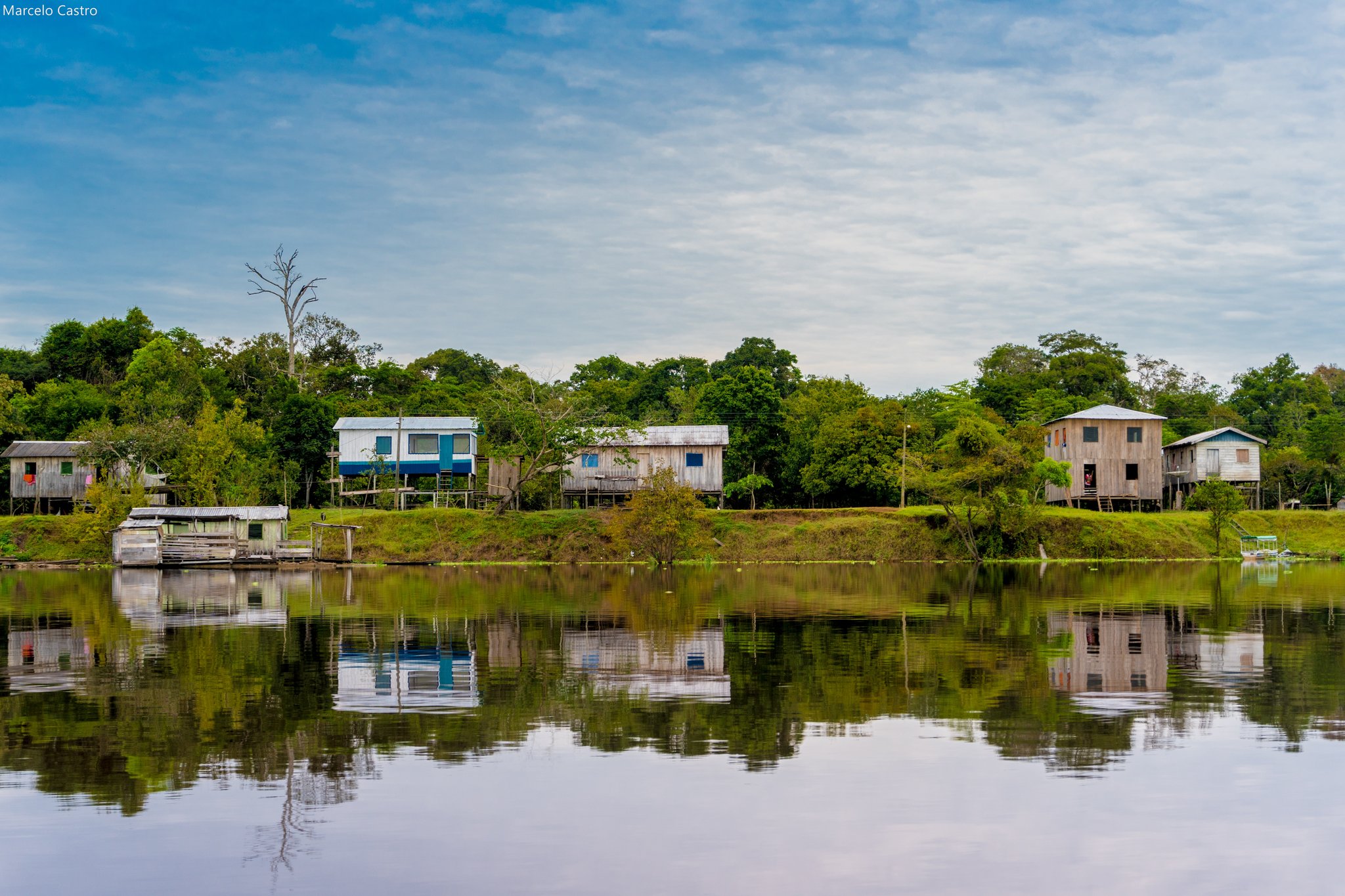 Hölzerne Pfahlhäuser spiegeln sich in einem ruhigen Flussarm, dahinter dichter Regenwald — eine Flussufergemeinschaft auf einer Amazonas-Regenwald-Ecolodge-Reise in Brasilien