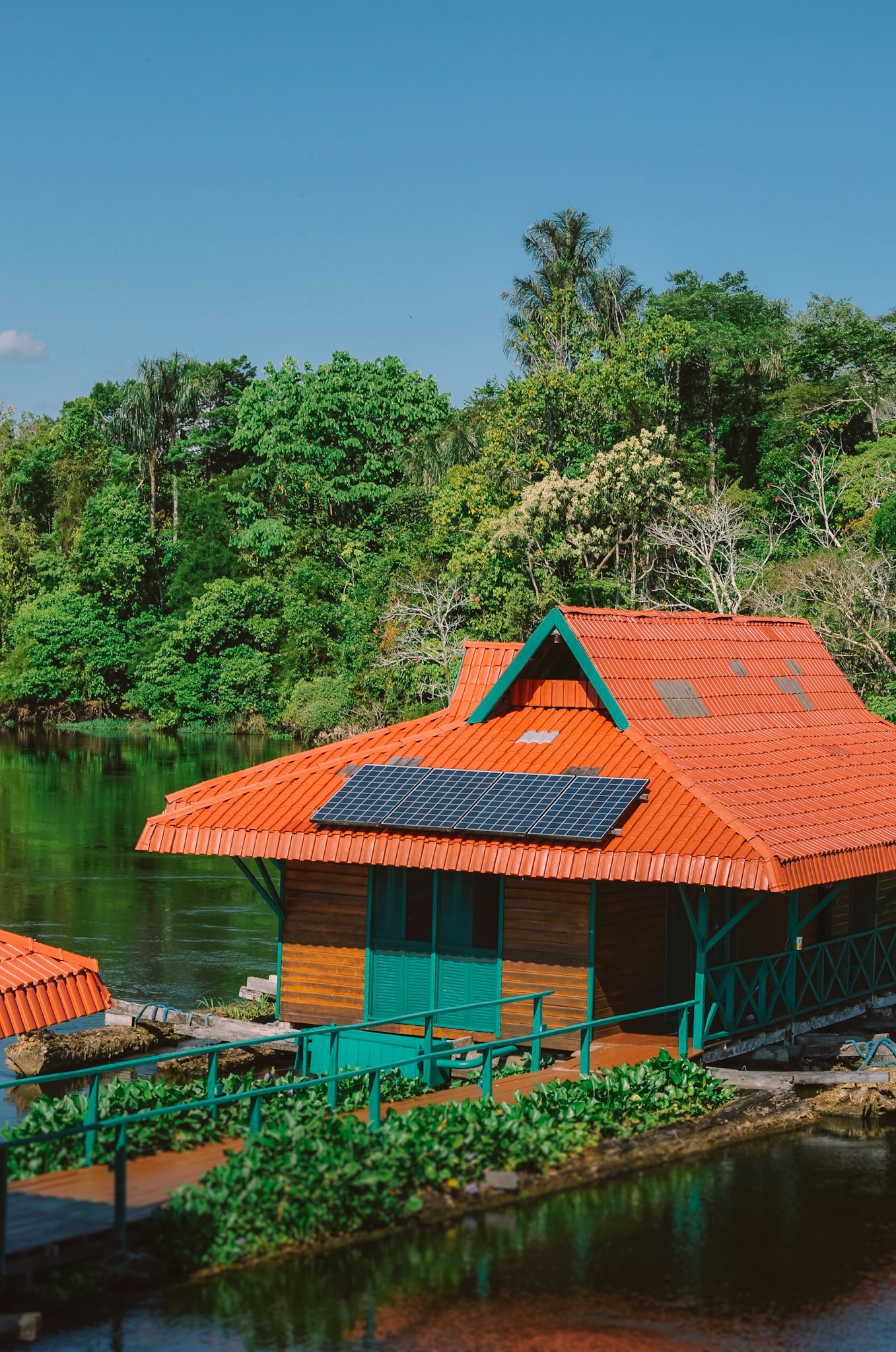 Eine schwimmende Holzhütte mit orangefarbenem Dach und Solarpaneelen auf einem dunklen Fluss, umgeben von tropischem Regenwald — Teil eines Amazon-Regenwald-Ecolodge-Trips in Brasilien