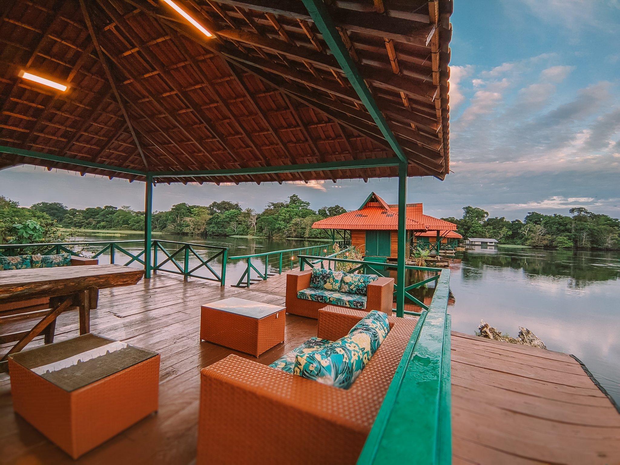 Überdachte Holzterrasse mit Rattanmöbeln und Blick auf einen ruhigen Fluss und dichten Regenwald in einem Amazon Rainforest Ecolodge in Brasilien