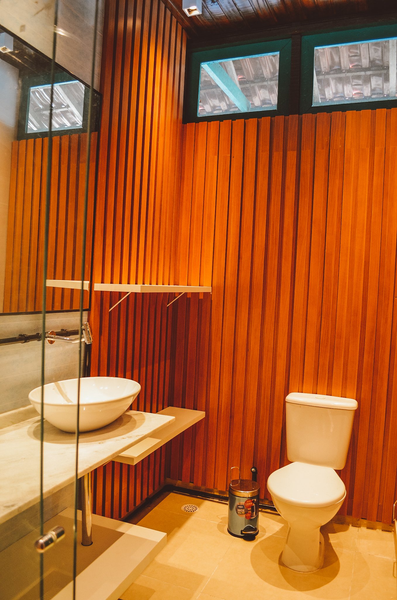 Private bathroom with warm timber slat walls, a bowl vessel sink on a marble countertop, and glass block windows at this amazon rainforest ecolodge trip in brazil