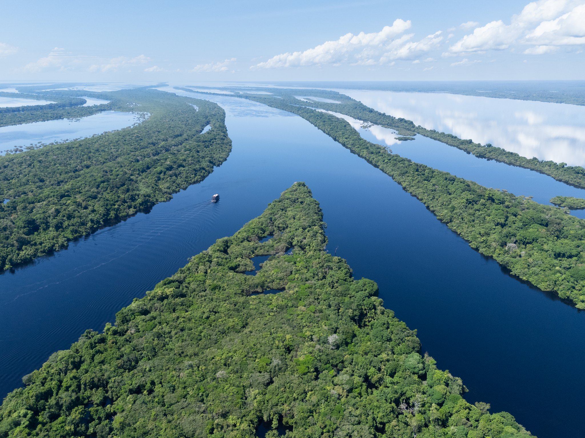 Vista aérea dos canais sinuosos do rio na floresta amazônica do Brasil, com ilhas de vegetação exuberante e uma pequena embarcação navegando nas águas escuras