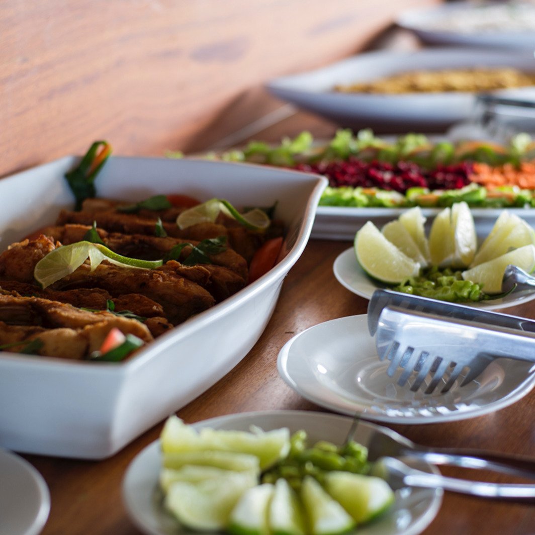Vibrant, fresh flavours straight from the rainforest kitchen. A generous buffet spread on an Amazon River Cruise Brazil table, featuring golden fried fish fillets garnished with lime, a colourful layered salad of beetroot, carrots and greens, fresh cucumber wedges, guacamole, and serving tongs on a warm wooden surface