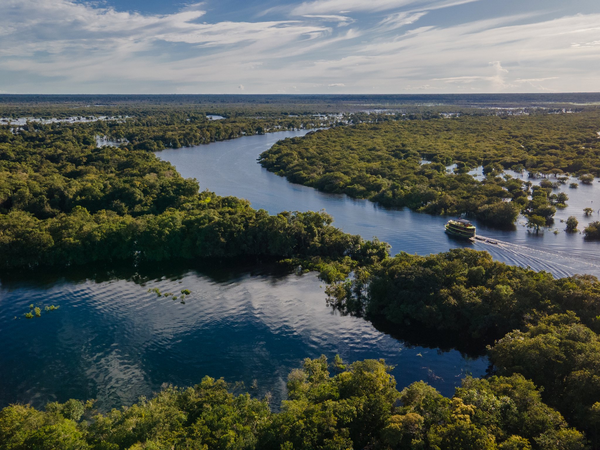An aerial view of a riverboat winding through the flooded forest and river channels of the Brazilian Amazon.