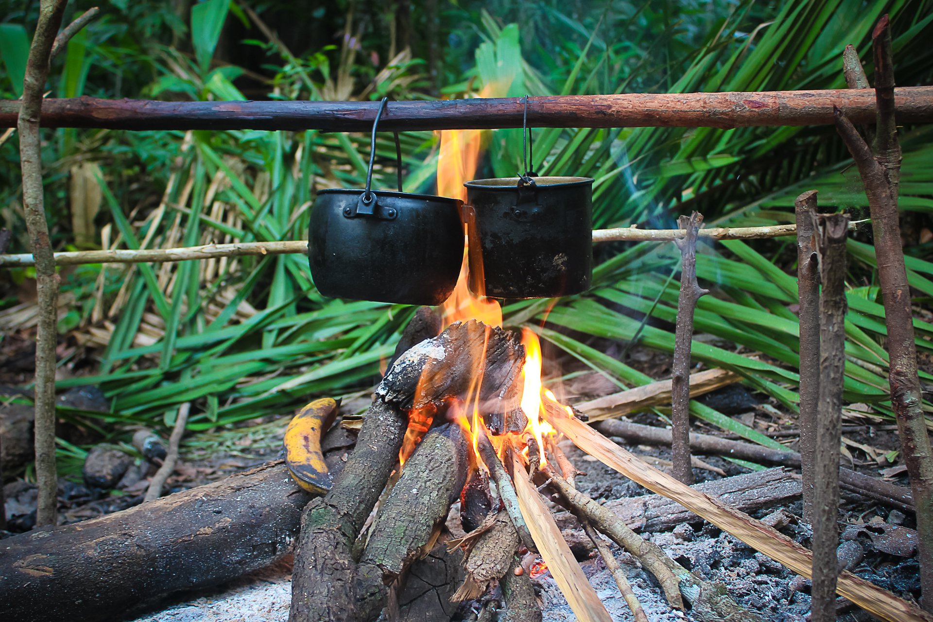 Eggs over open flame — camp cooking stripped back to its essentials. Photo: Joshua Lacruz Two blackened pots hanging over an open wood fire on a jungle survival Brazil camp, one holding eggs boiling in water