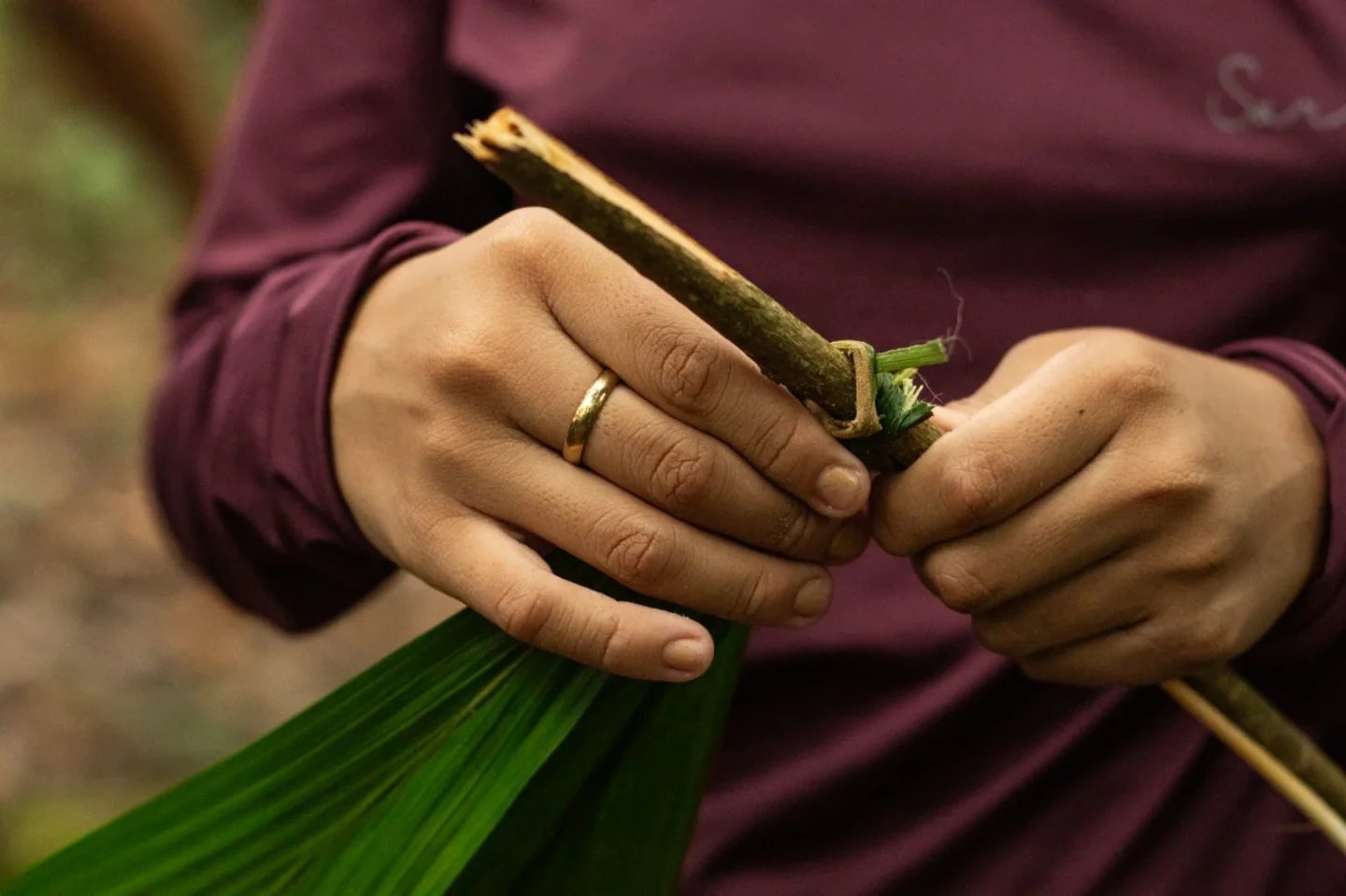 The forest gives you everything, if you know how to ask. Close-up of hands binding a wooden stick to green palm fronds during an Amazon trek and survival tour jungle craft demonstration