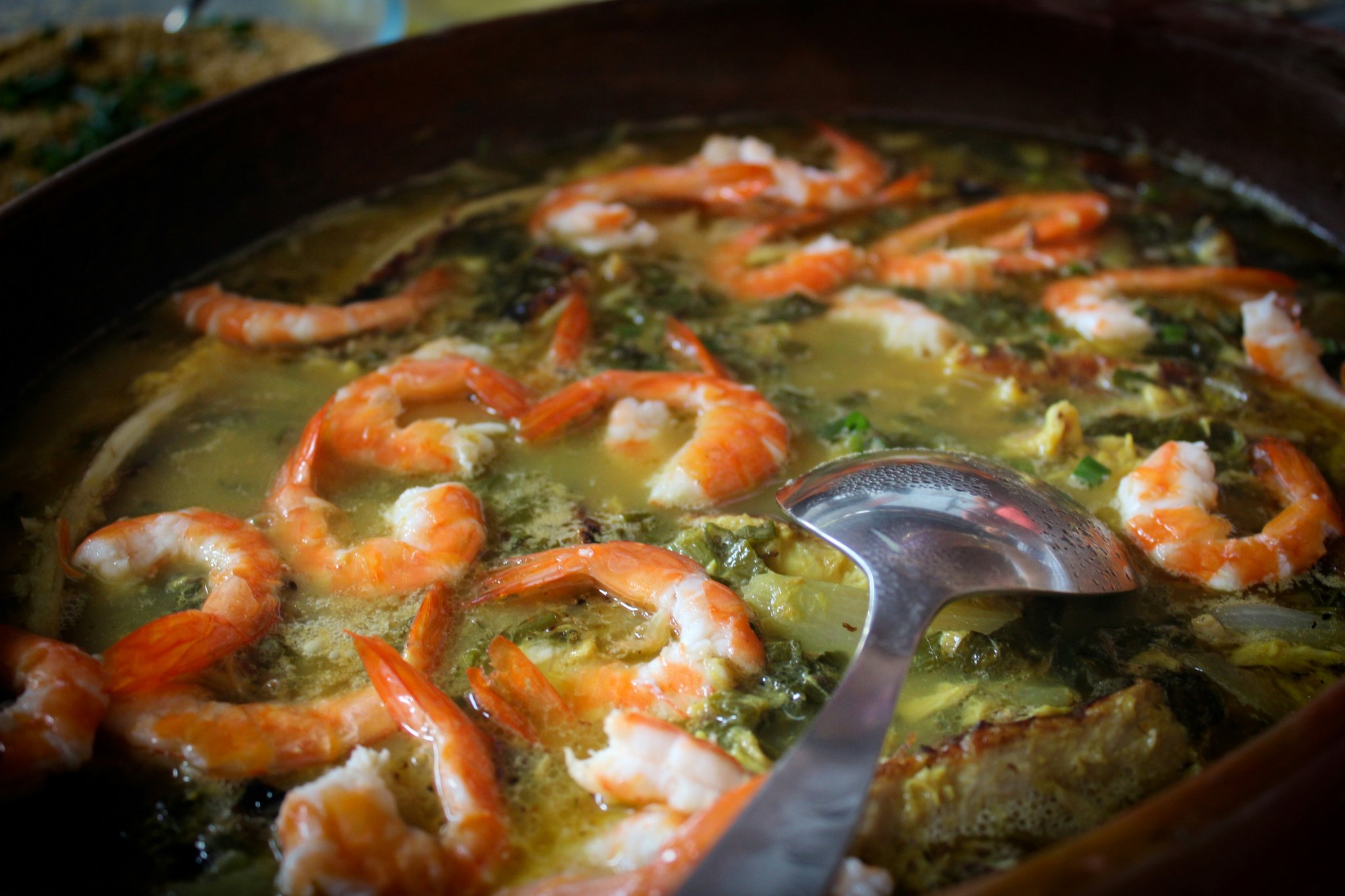 Clay pot of Amazonian shrimp and jambu stew in golden tucupi broth with a serving ladle
