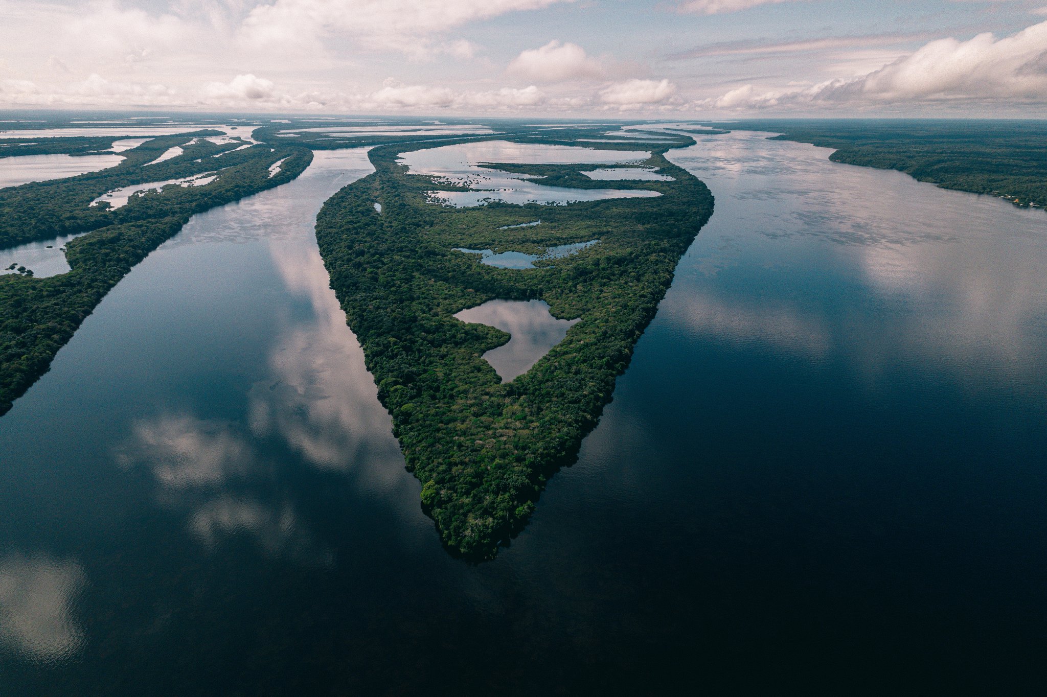 Aerial view of a densely forested island at Anavilhanas Jungle Lodge Brazil, surrounded by the dark mirror-calm waters of a vast river archipelago under a cloudy sky