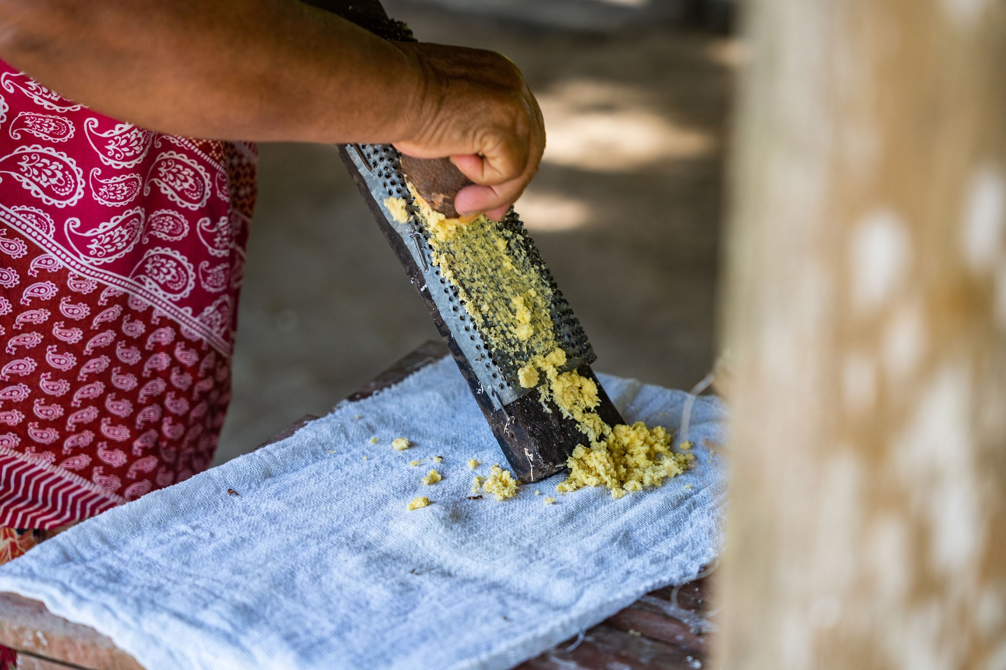 A local woman in a red patterned apron grating fresh cassava onto a cloth at the Anavilhanas Jungle Lodge Brazil riverside community visit