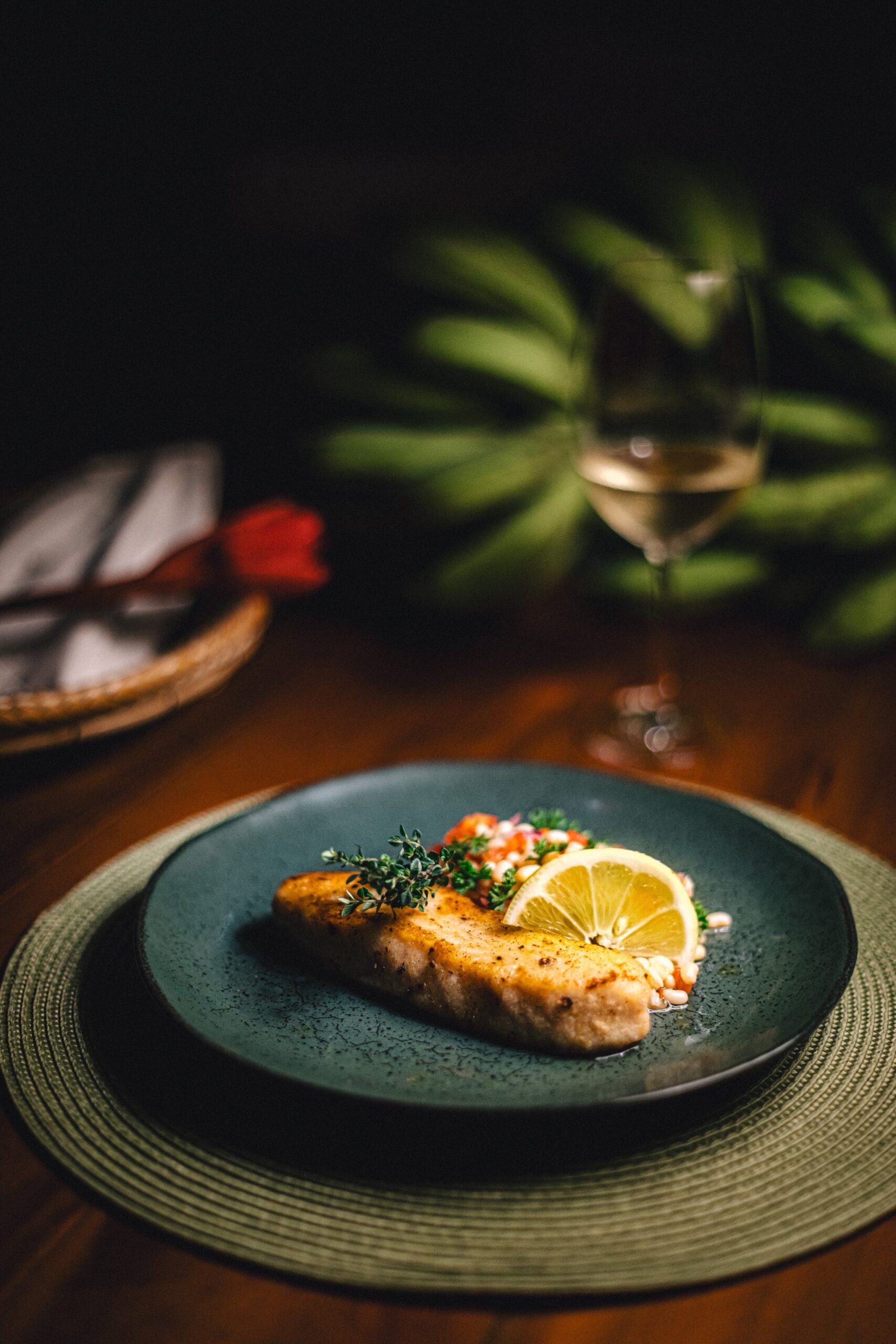 Freshwater flavours, plated with care — dinner in the heart of the Amazon. A pan-seared fish fillet garnished with fresh herbs and a lemon slice on a dark ceramic plate at Anavilhanas Jungle Lodge Brazil, served alongside a glass of white wine