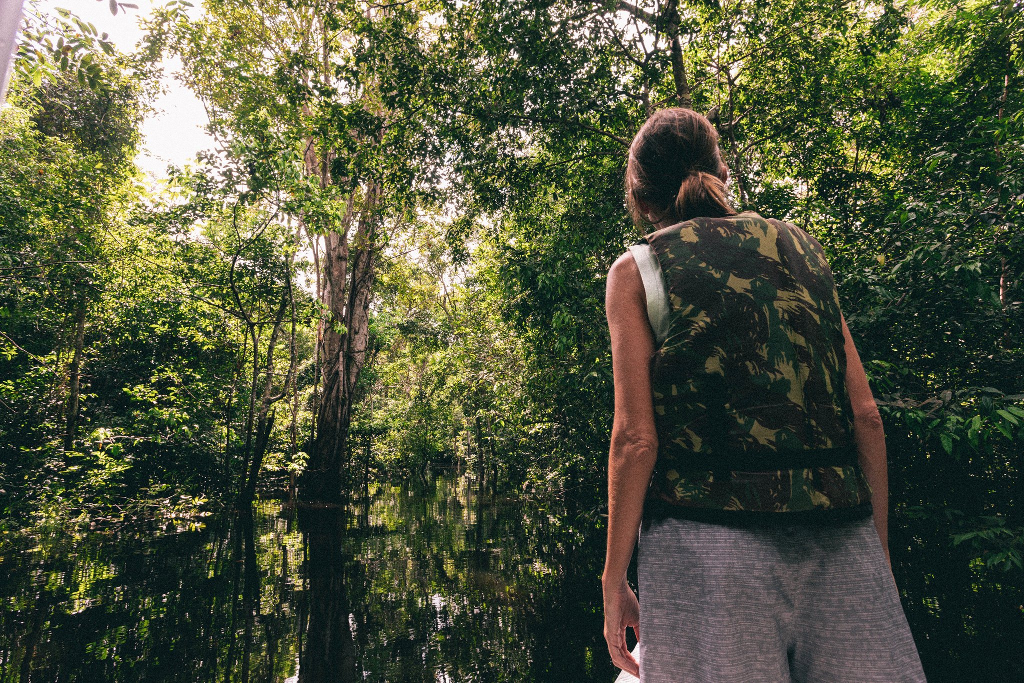 A traveller in a camouflage vest gazes into a flooded igapó forest at Anavilhanas Jungle Lodge Brazil, dark still water reflecting tall green trees