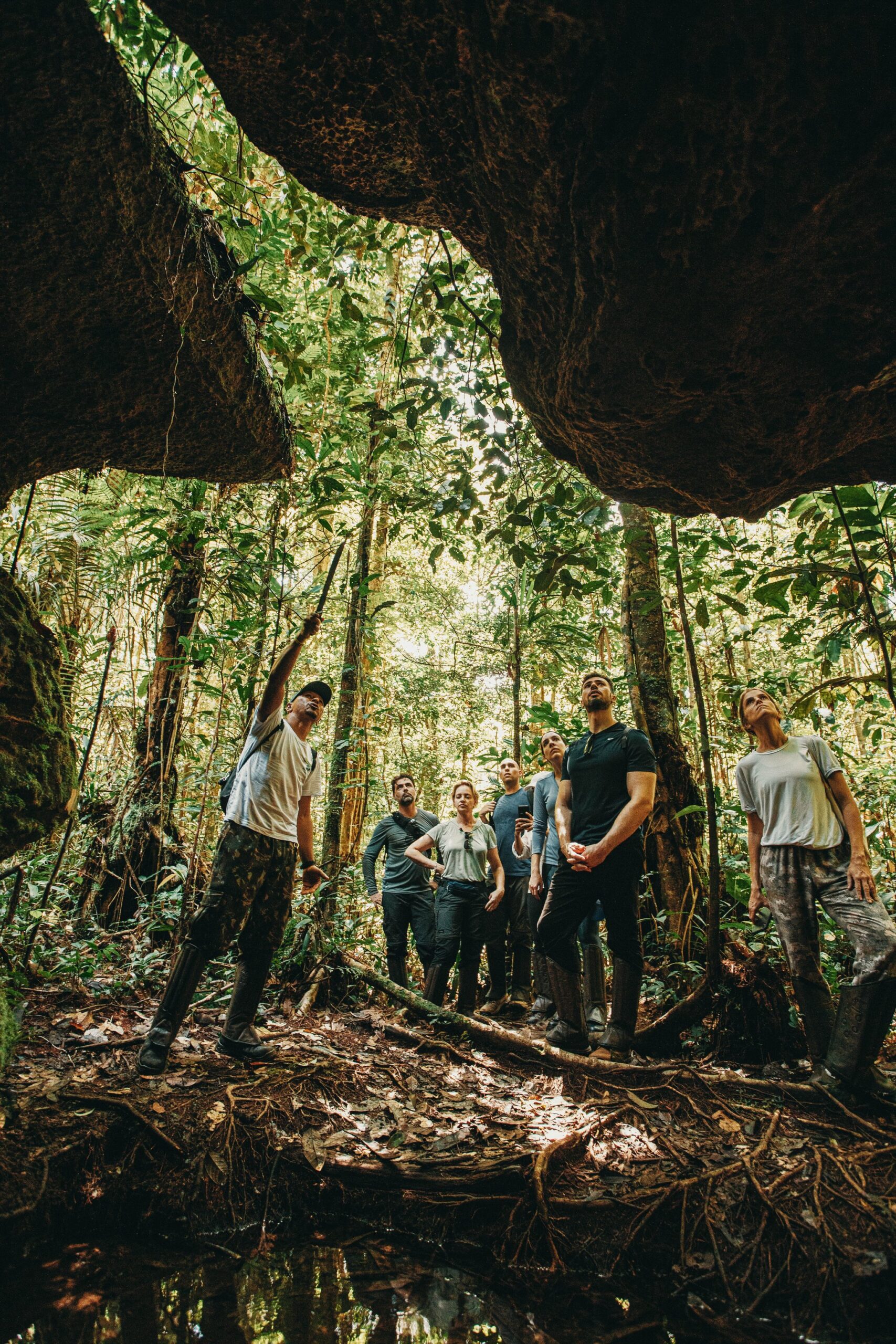 A guide points upward while a small group of travellers gazes toward the rainforest canopy, framed by the ancient rock arch of a cave at Anavilhanas Jungle Lodge Brazil