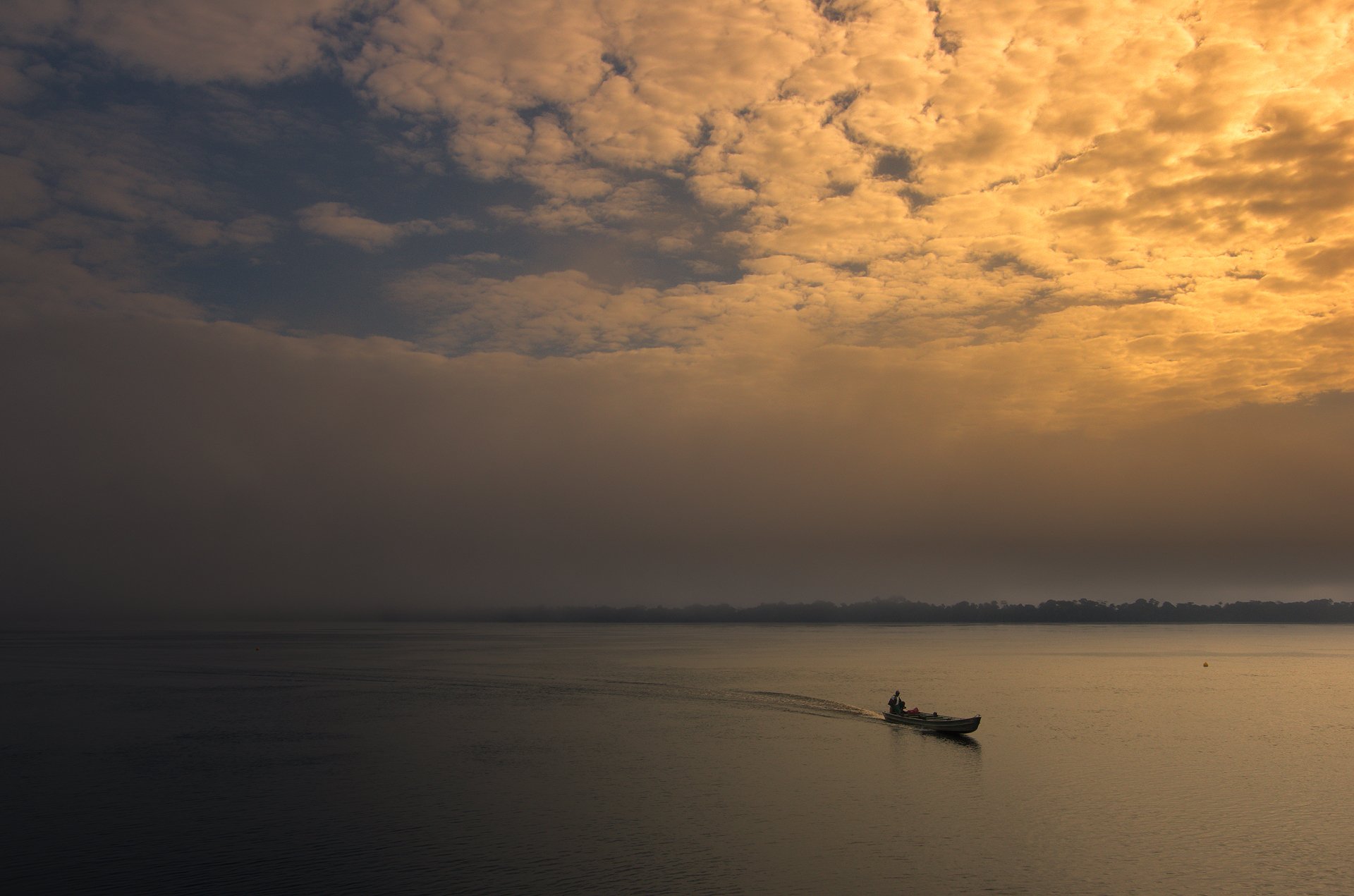 A small motorboat leaving a gentle wake across the glassy Rio Negro at dusk, beneath a dramatic sky of amber and gold clouds, near Anavilhanas Jungle Lodge Brazil