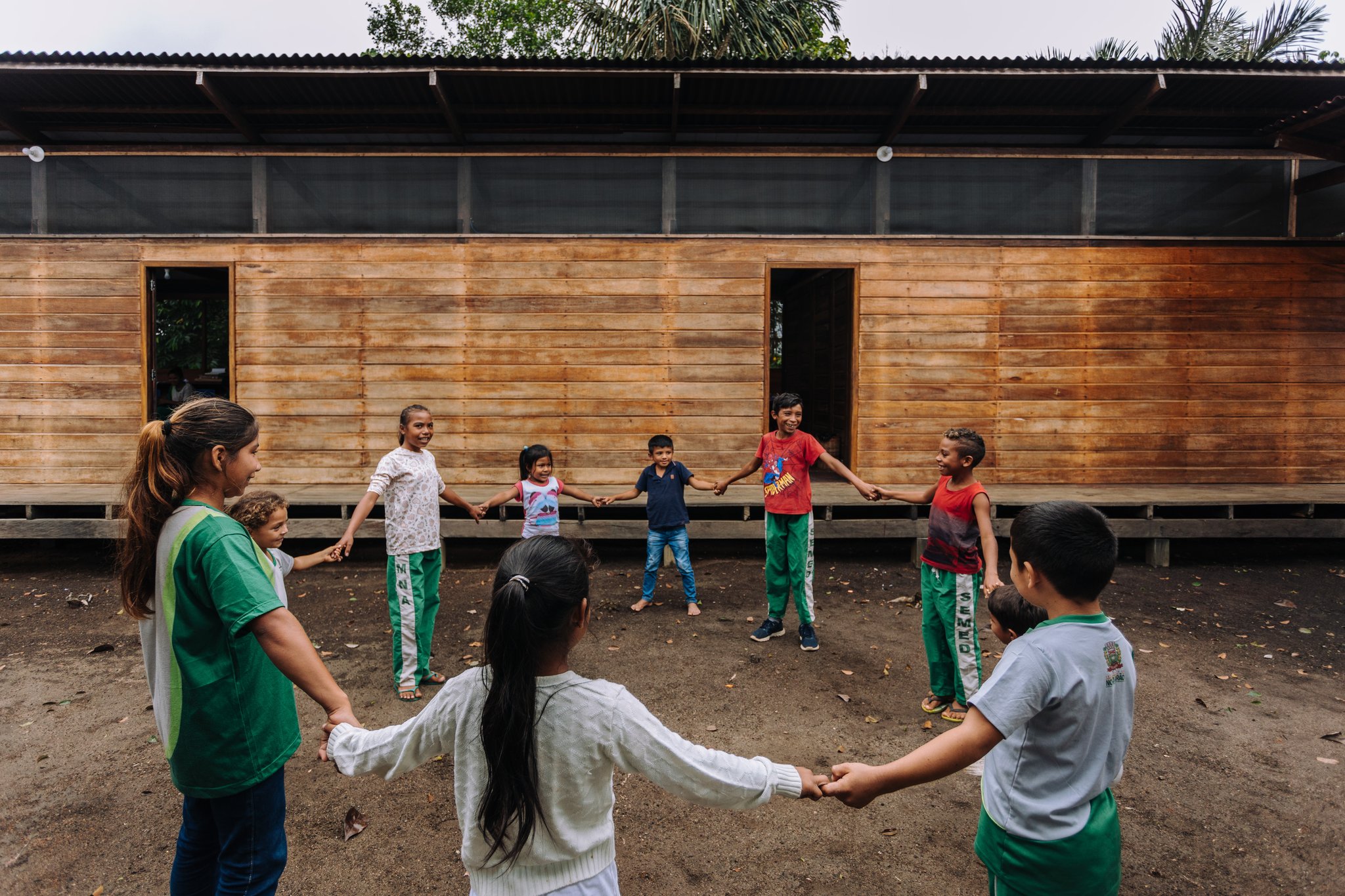 Children holding hands in a circle and playing outside a wooden community building during a riverside village visit at Anavilhanas Jungle Lodge Brazil