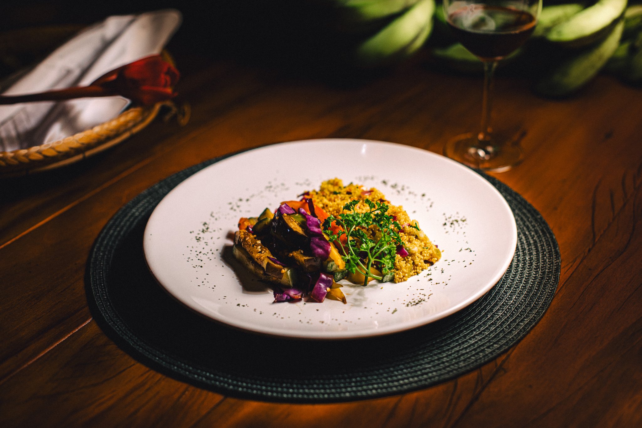 Colourful, careful, and utterly satisfying after a day in the rainforest. A plated dinner at Anavilhanas Jungle Lodge Brazil featuring roasted vegetables, golden couscous and fresh herbs on a white dish, with a glass of red wine in the background